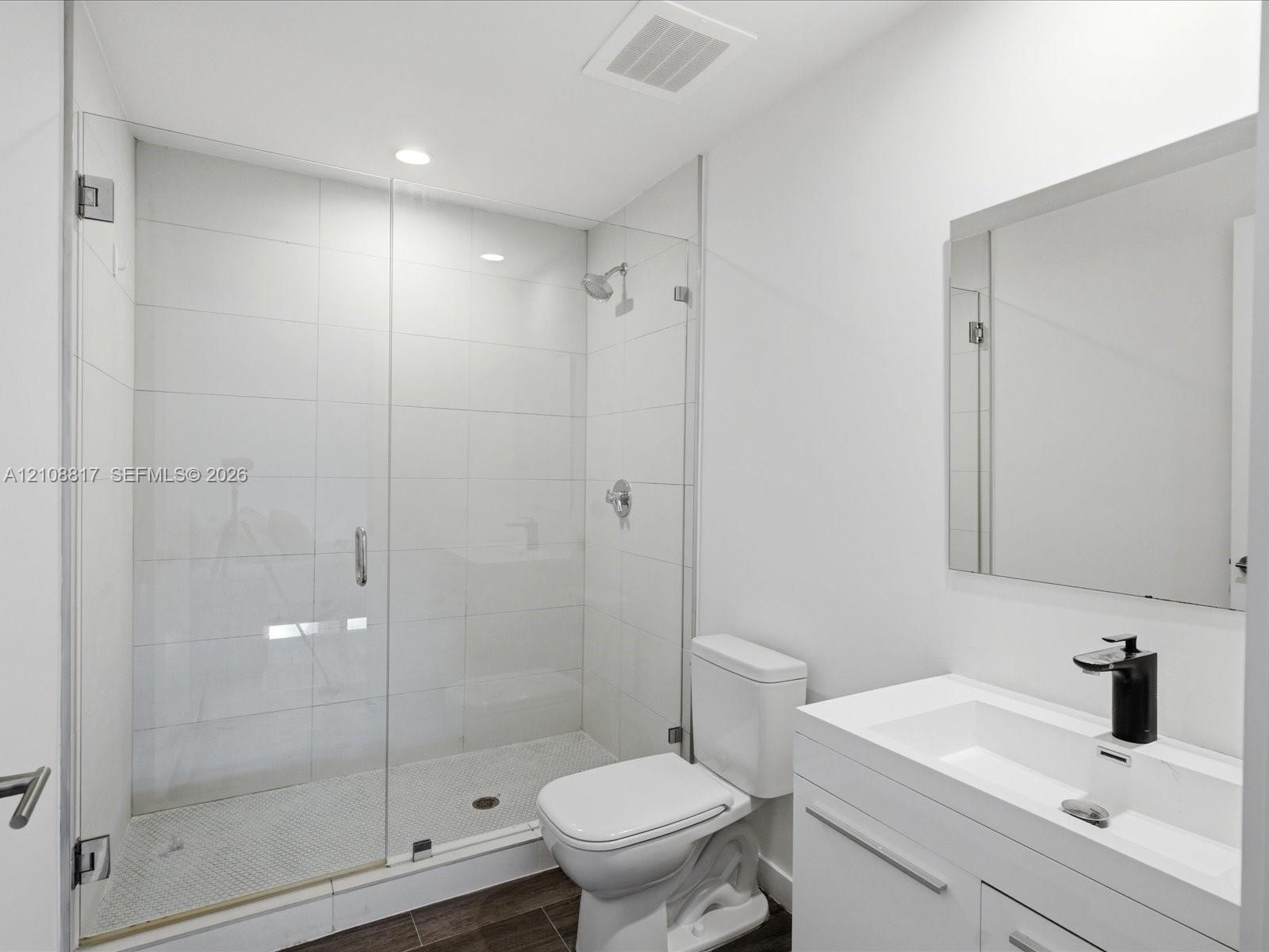 Walk-in shower with a glass enclosure, floor-to-ceiling white tile, modern vanity with a rectangular sink, matte black faucet, and polished mirror