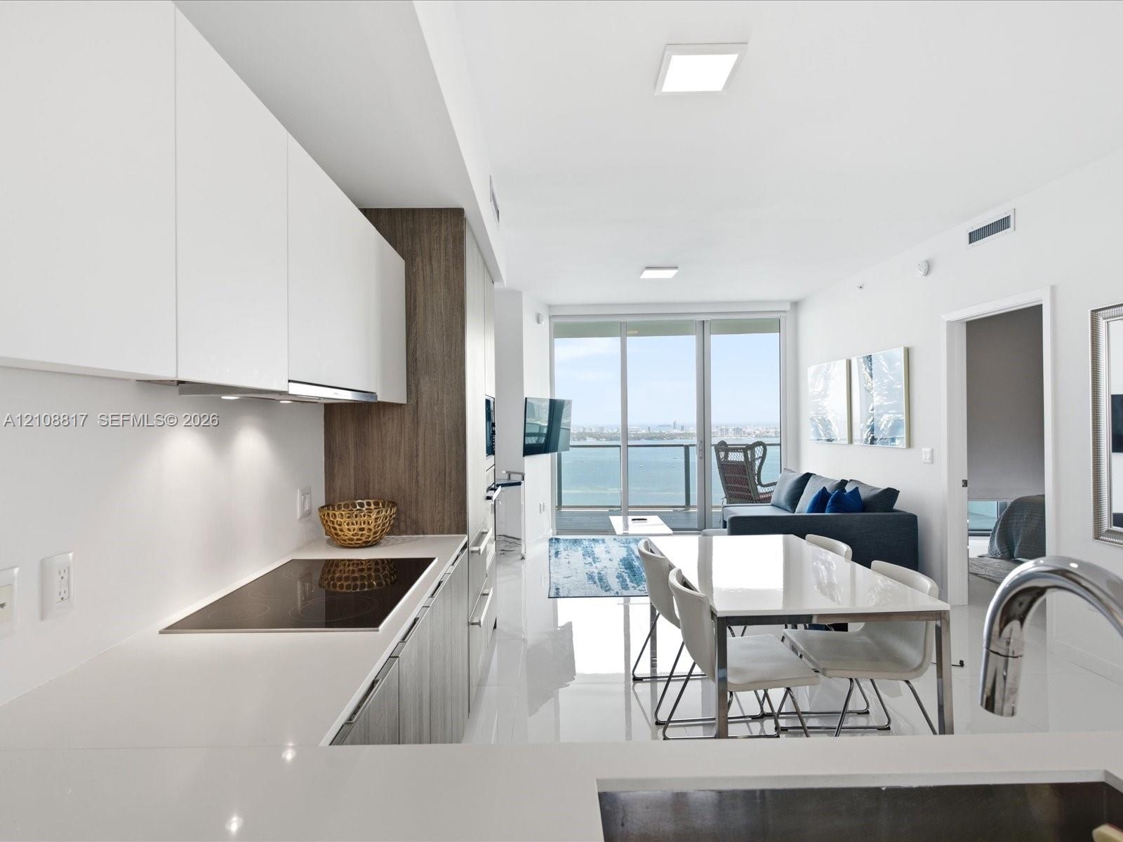 Modern kitchen featuring flat-panel cabinetry, light-toned countertops, built-in cooktop, and large-format tile flooring, accented by floor-to-ceiling