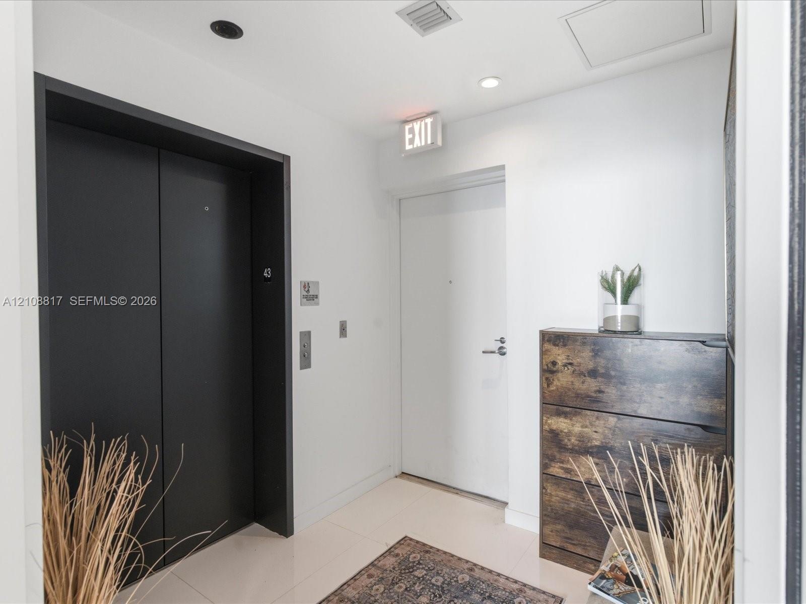 Entryway featuring a matte black elevator facade, solid-core interior door with brushed metal hardware, and neutral tile flooring