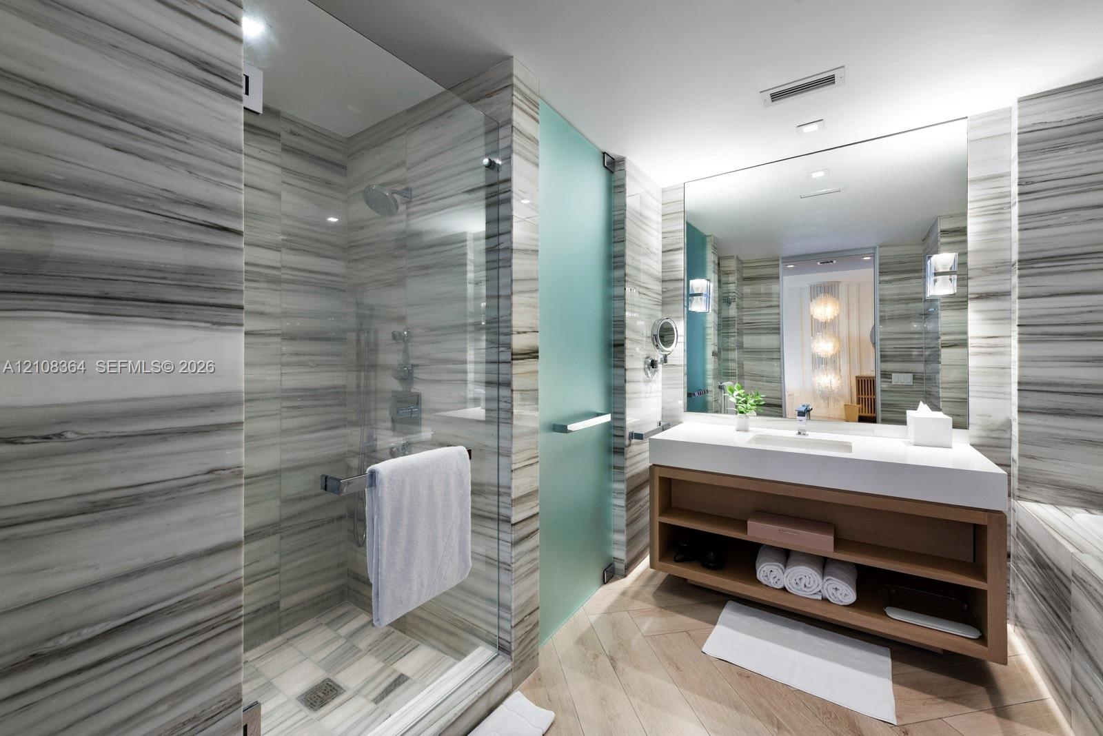 Bathroom featuring floor-to-ceiling stone-tiled walls, a walk-in shower with a glass enclosure, a floating vanity with open shelving, a large wall-mou