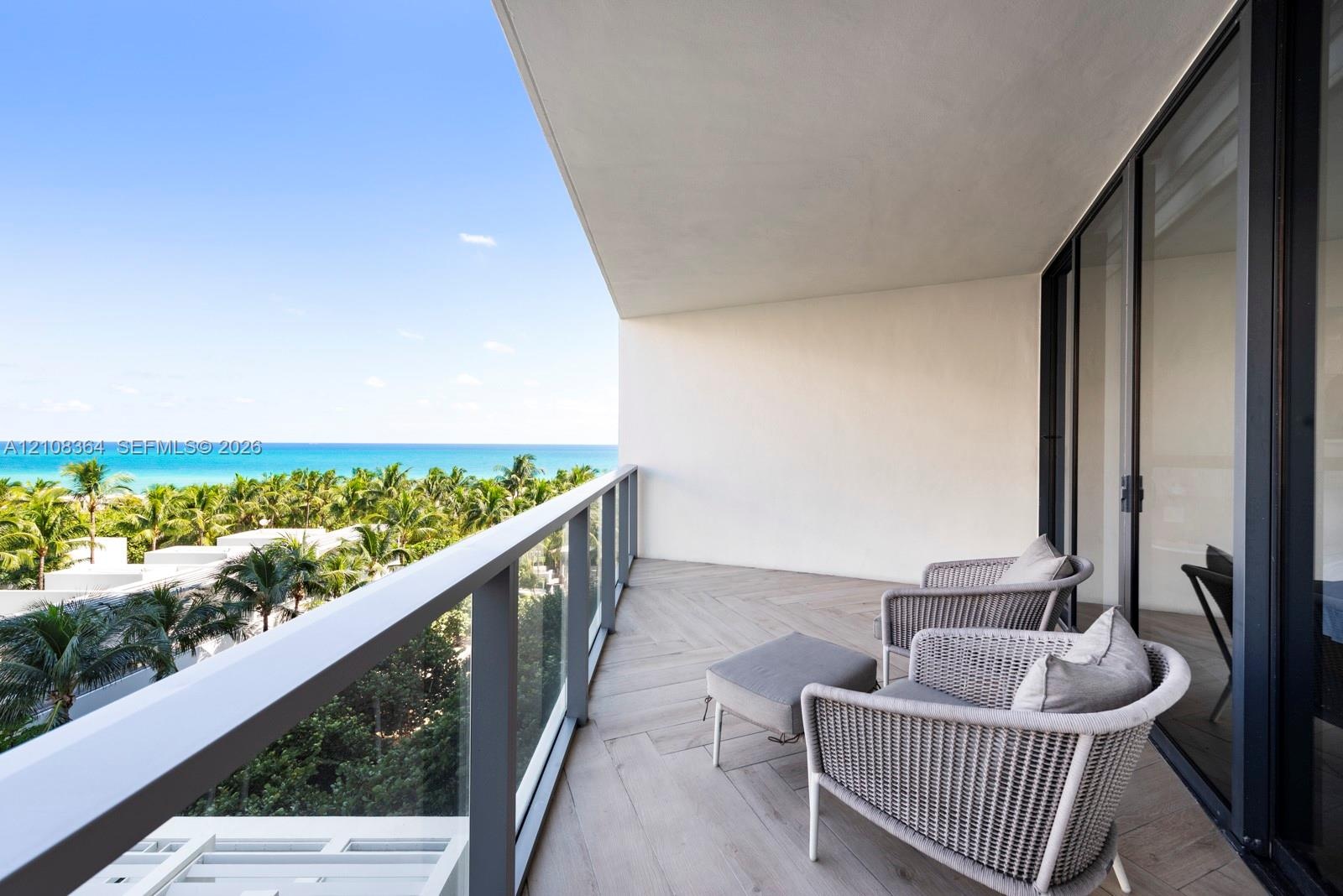 Private covered balcony featuring herringbone-patterned flooring, glass-paneled railing, and expansive ocean scenery