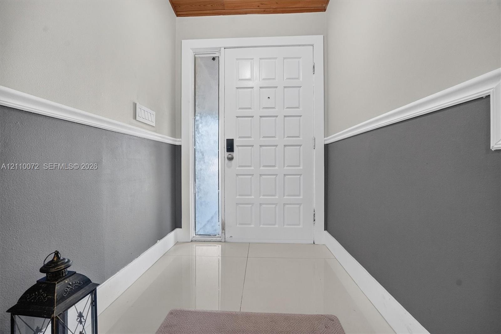 Entryway featuring a grid-patterned door with a vertical glass side panel, two-tone wall finish with decorative chair rail molding, and large-format t