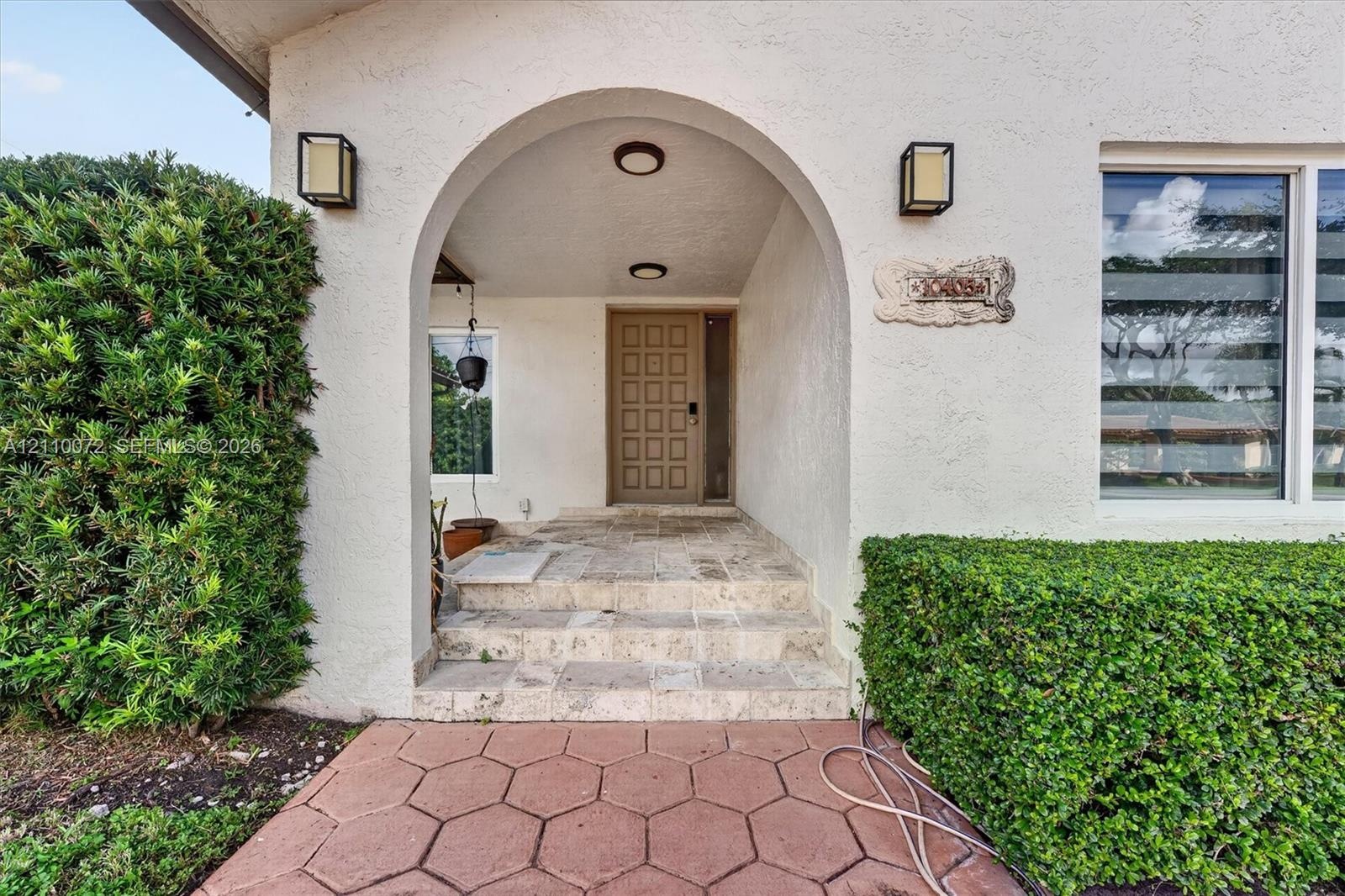Covered entryway featuring a stone-stepped porch, arched architectural detail, square-paneled front door, and metal wall-mounted light fixtures