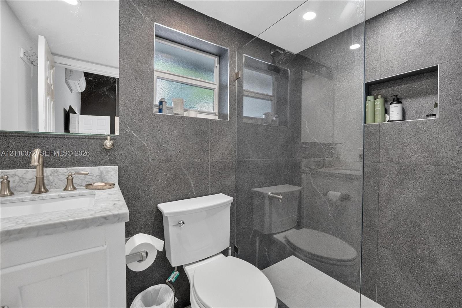 Bathroom featuring large-format dark stone wall tile, glass-enclosed shower with built-in recessed niche, stone-topped vanity with metallic faucet, an