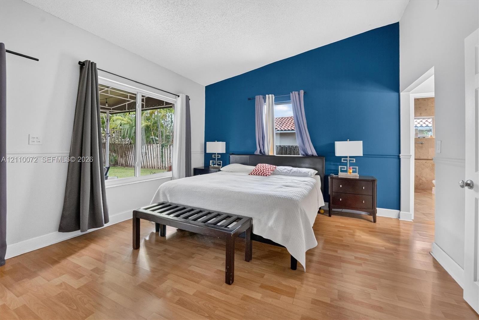 Vaulted ceiling, wood-finish flooring, accent wall, and large windows with outdoor exposure