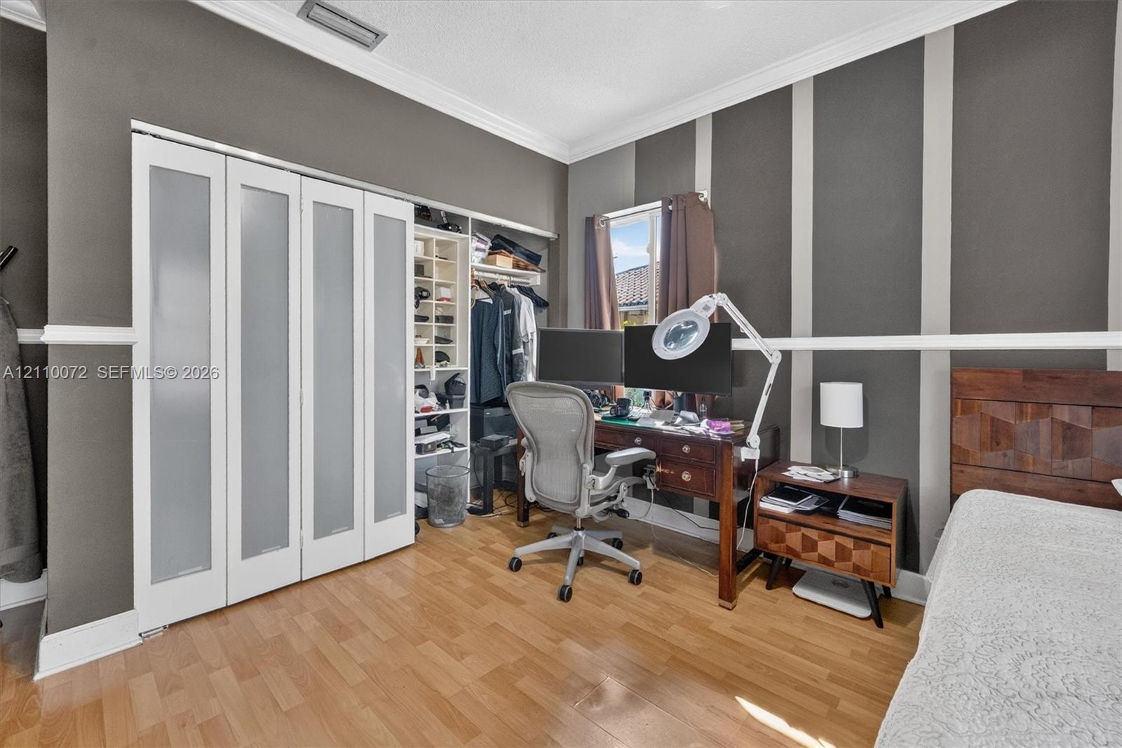Room featuring wood-finish flooring, crown molding, chair rail trim, and a built-in closet system with frosted glass panels