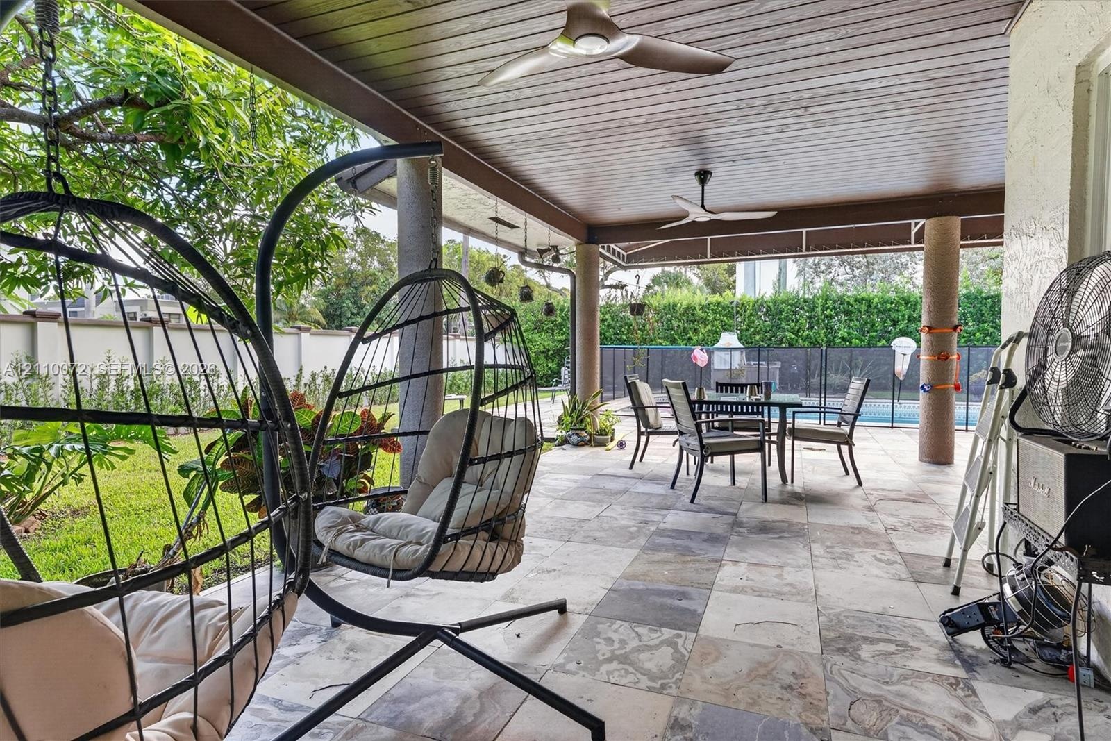 Covered patio featuring stone-tile flooring, wood-paneled ceiling, integrated ceiling fans, and structural columns