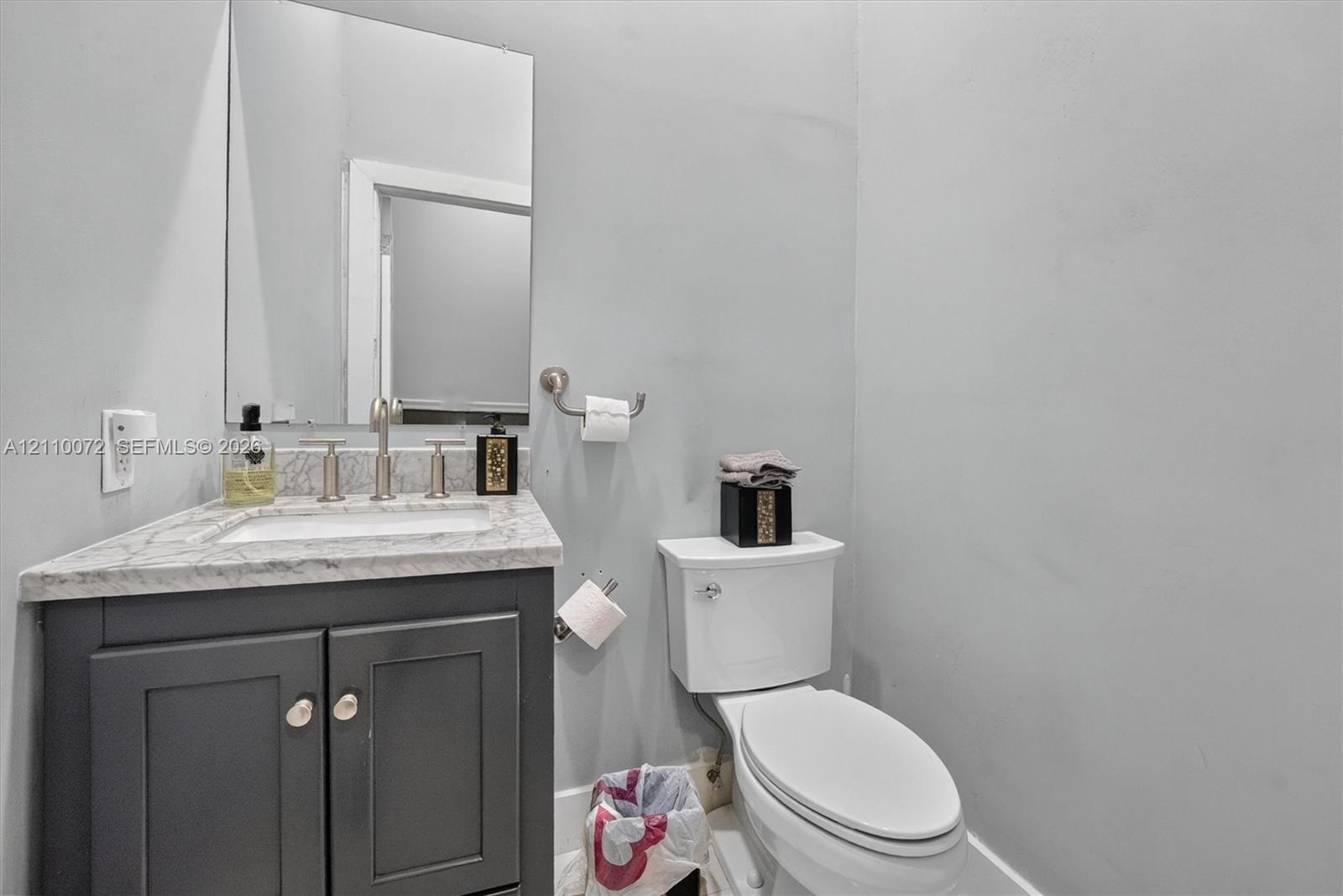 Dark-finished vanity with stone-surface countertop, rectangular undermount sink, brushed-metal faucet, and frameless wall-mounted mirror