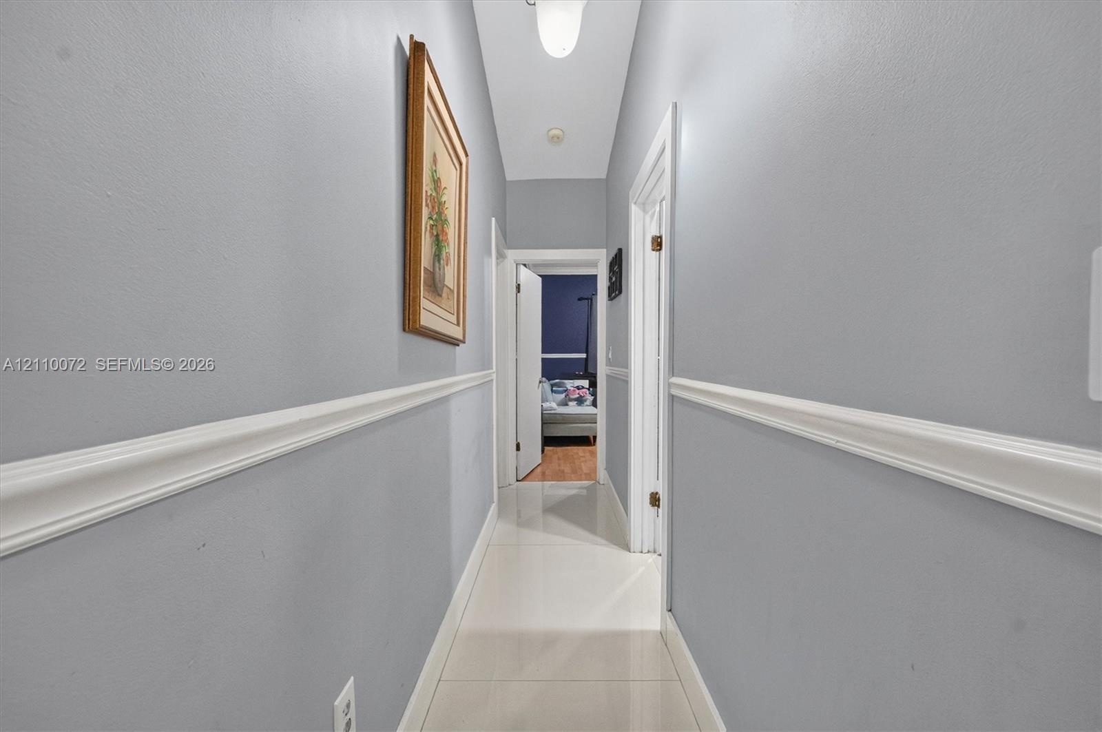 Hallway featuring light-toned tile flooring, chair rail molding, and crisp white door casings