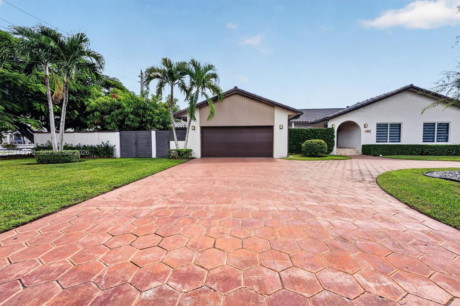 Single-story residence featuring a hexagonal paver driveway, an attached garage, and manicured landscaping with palm trees