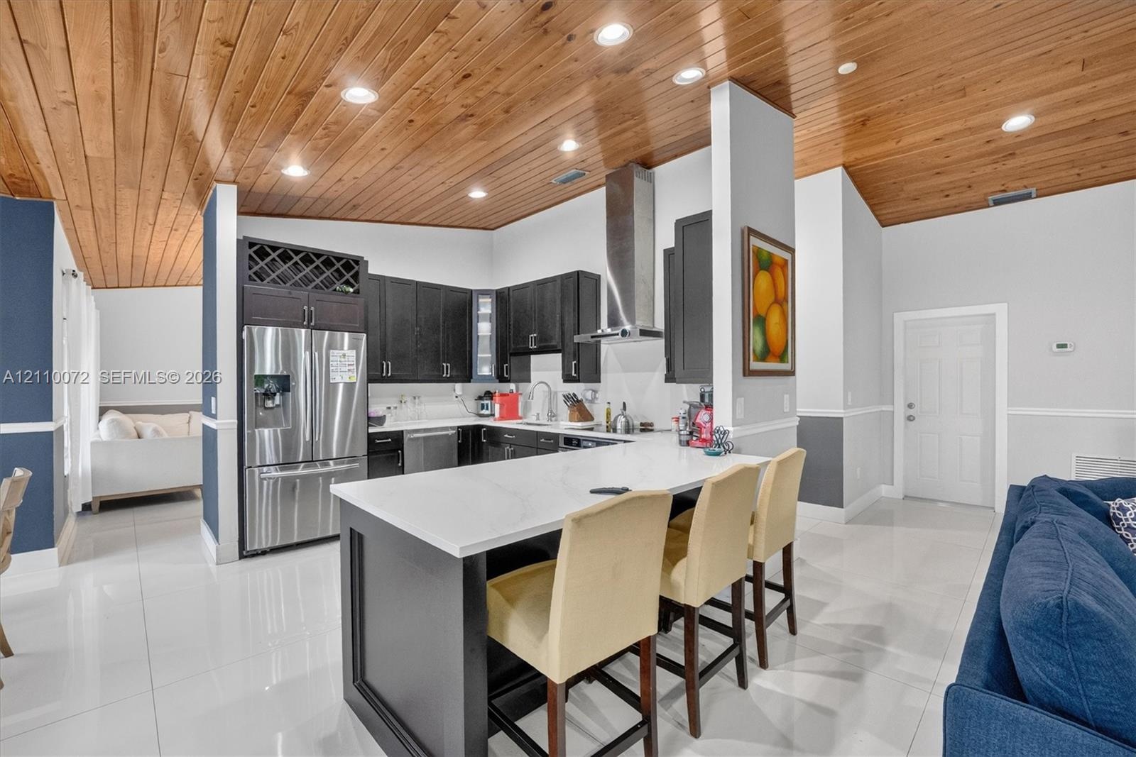 Kitchen featuring vaulted wood-plank ceilings, a central island with a solid-surface countertop, dark-toned cabinetry, stainless steel appliances, and