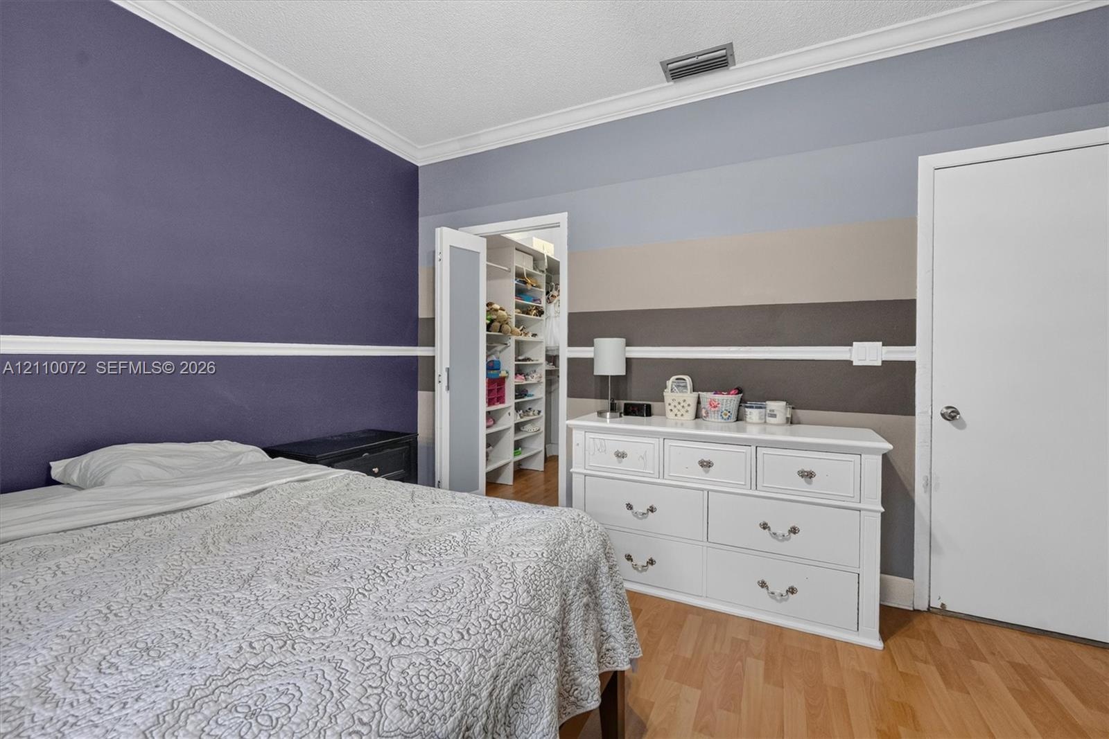 Room featuring wood-finish flooring, crown molding, and a walk-in closet with built-in shelving