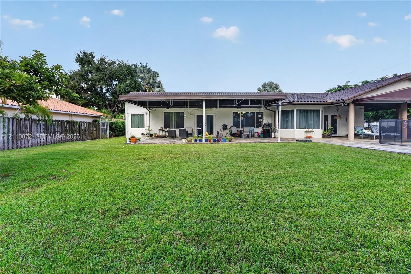 Expansive backyard featuring a manicured lawn, full-width covered patio, tile roof, and privacy fencing