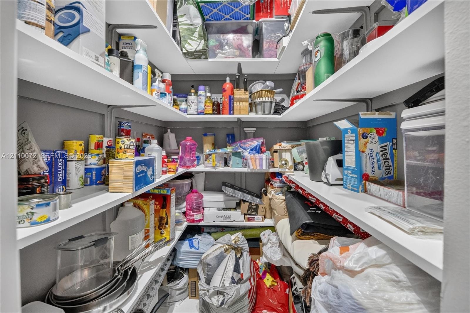 Walk-in storage pantry featuring U-shaped white shelving and wall-mounted metal support brackets