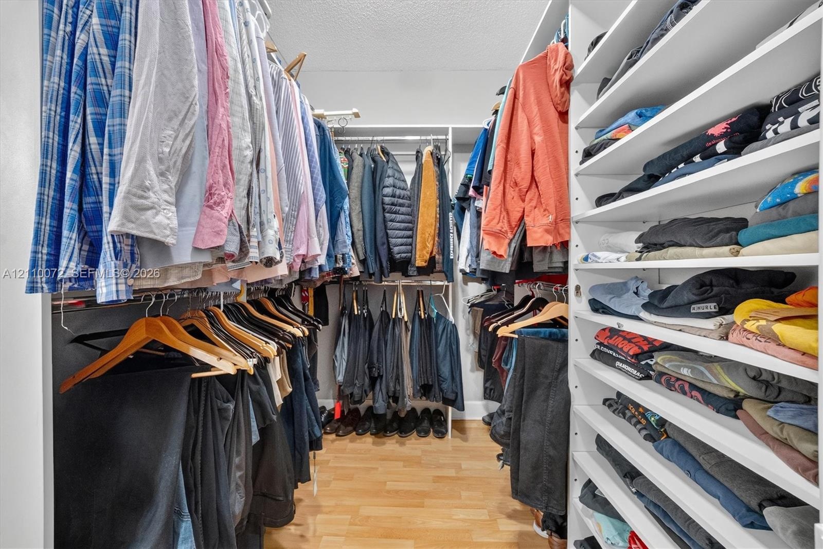 Walk-in closet featuring extensive built-in white shelving, multiple hanging rods, and wood-finish flooring