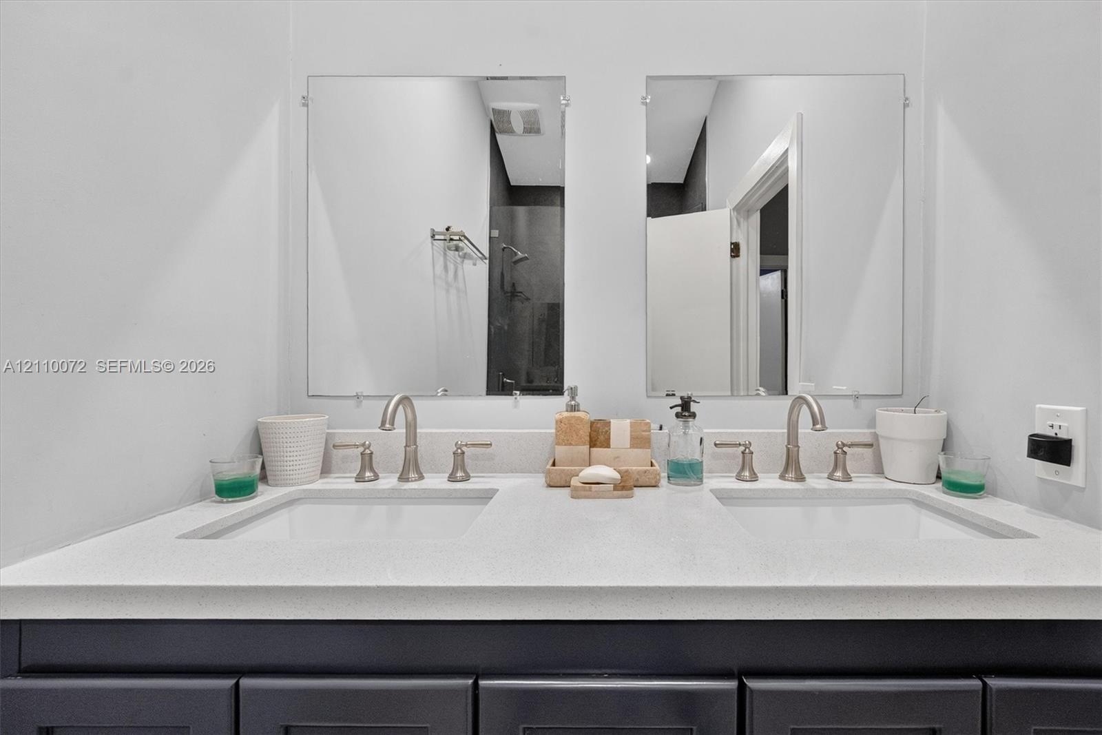 Dual-sink vanity with white stone countertop, rectangular undermount basins, brushed nickel widespread faucets, and twin frameless mirrors