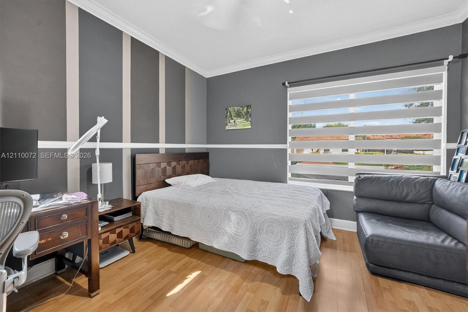Bedroom featuring wood-finish flooring, accent-painted walls with chair rail molding, crown molding, and horizontal privacy shades