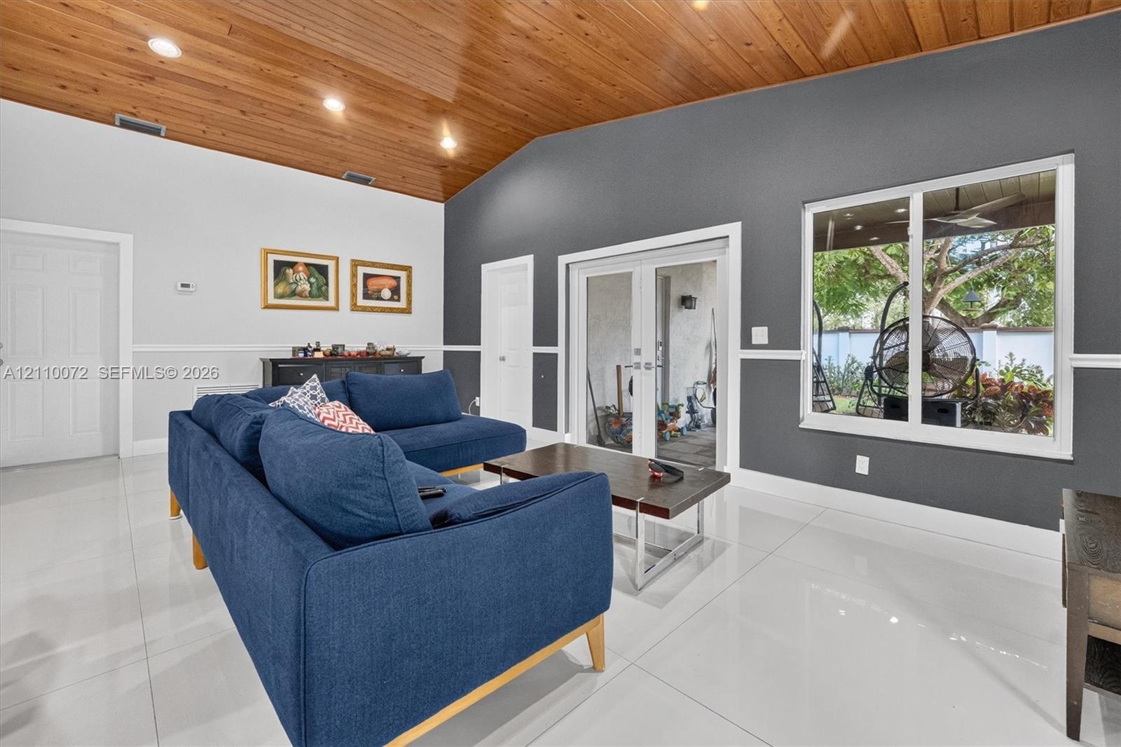 Vaulted ceiling with wood-plank finish, recessed lighting, large-format tile flooring, and dual glass-panel patio doors