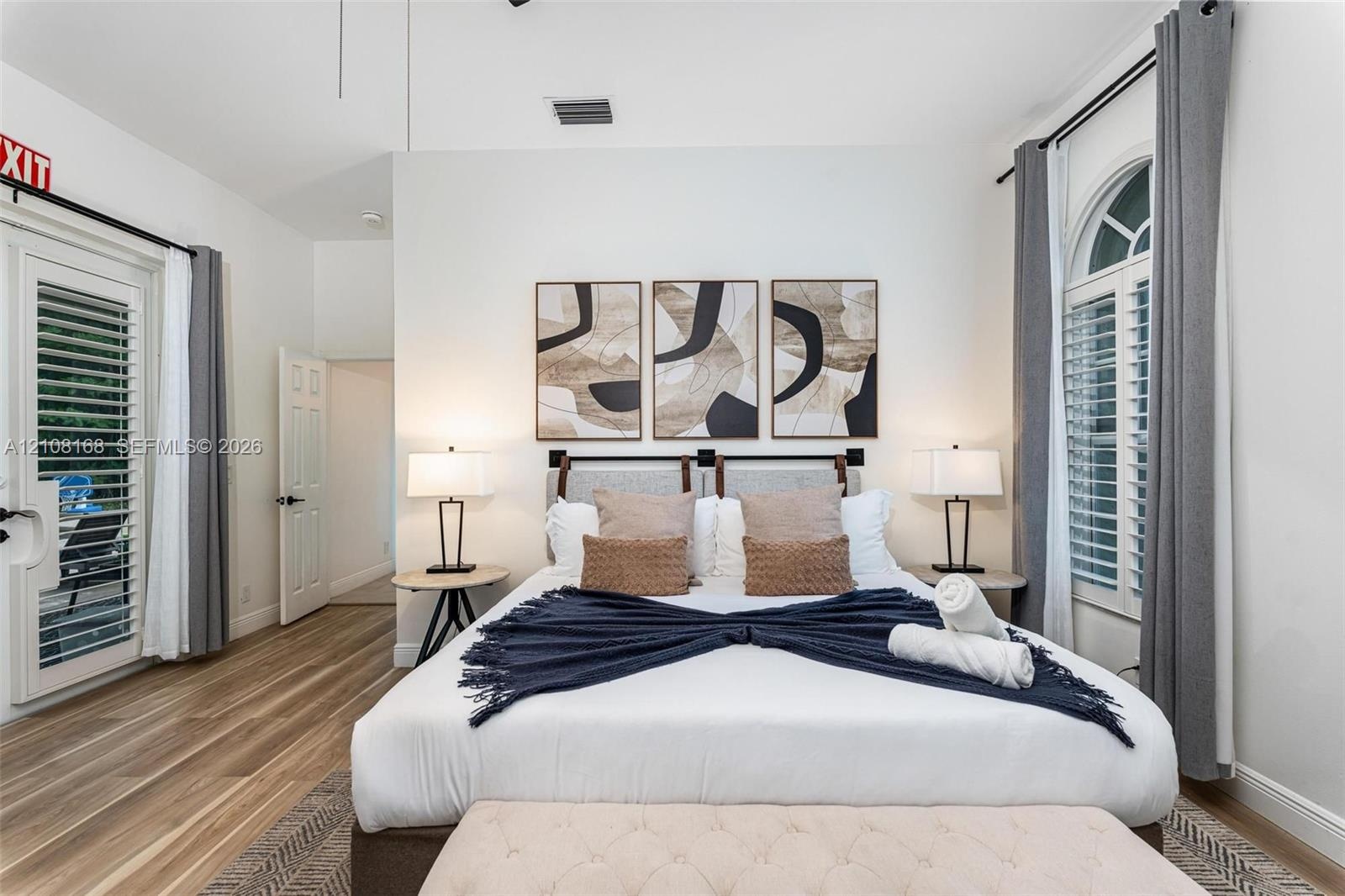 Wood-finish flooring, high ceilings, arch-top window with plantation shutters, and a glass-paneled exterior door