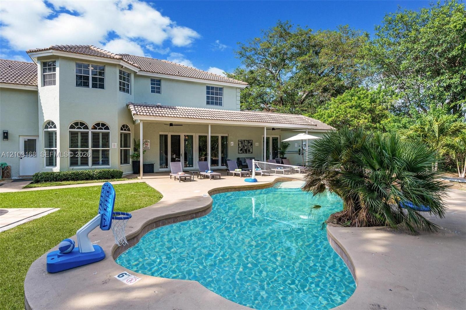 Two-story residence featuring a tile roof, covered rear patio, free-form pool, and manicured landscaping