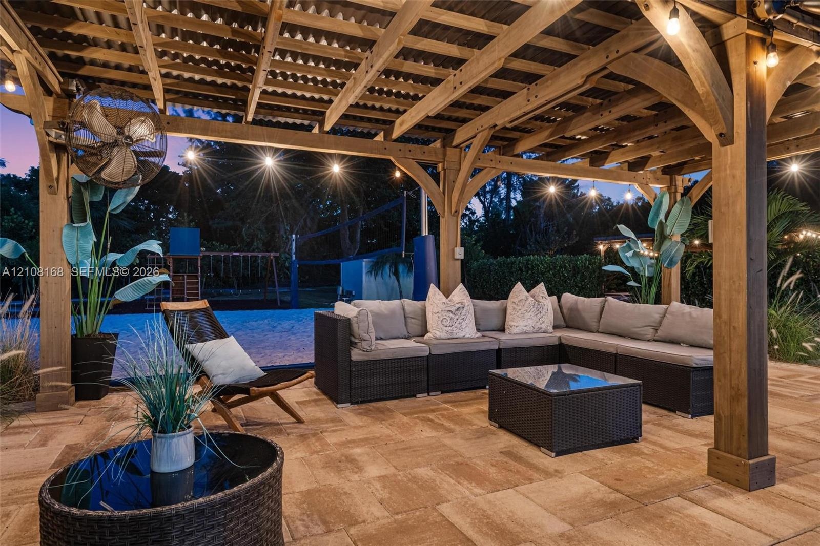Covered timber-frame pergola featuring exposed rafters, stone-paver flooring, a ceiling-mounted fan, and string lighting