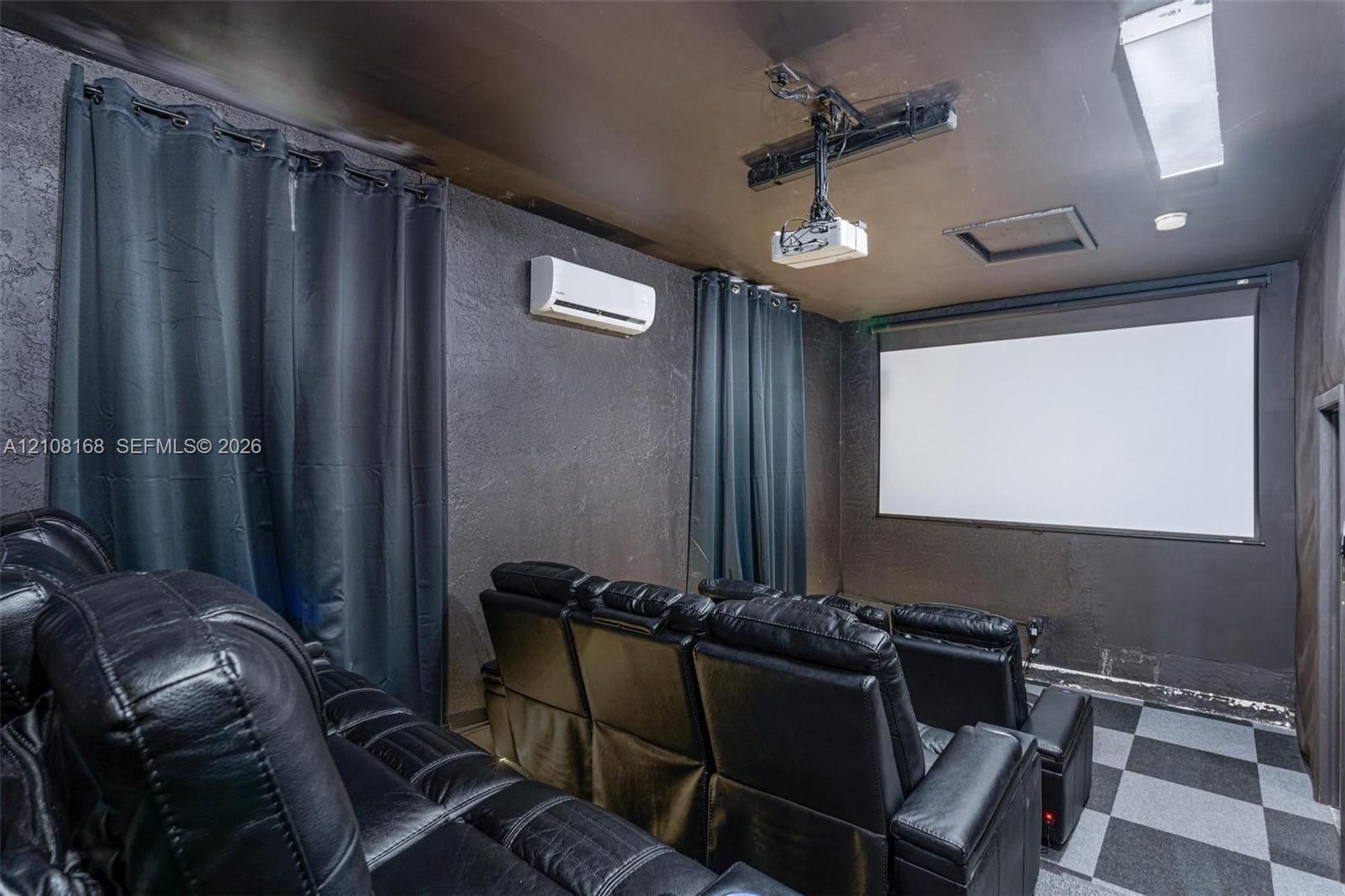 Media room featuring a mounted projection screen, ceiling-mounted digital projector, wall-mounted ductless air conditioning unit, and checkered tile f