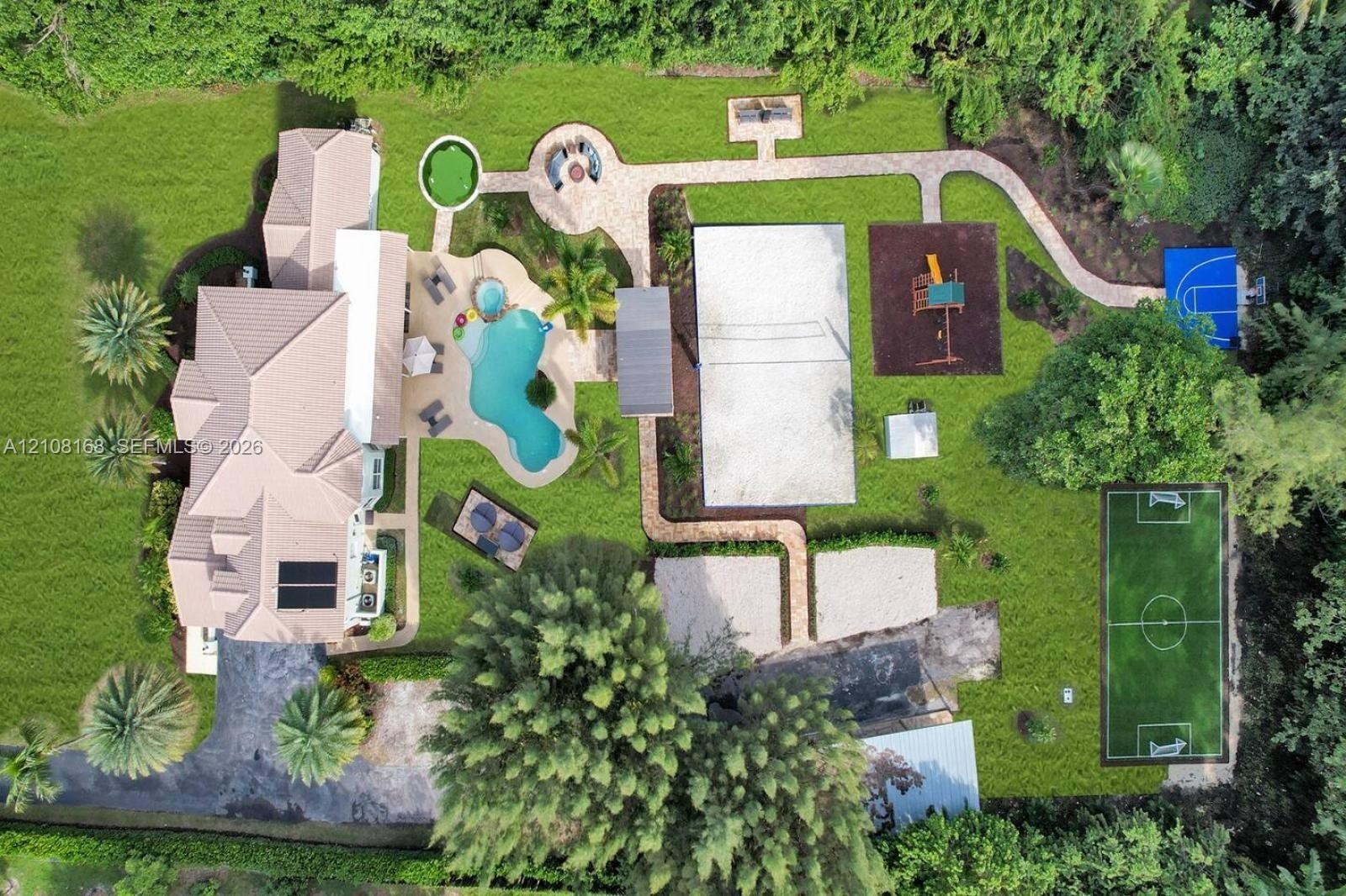 Expansive backyard featuring a custom-shaped swimming pool with an attached spa, a sand volleyball court, a soccer field, a paved walking path, and a 