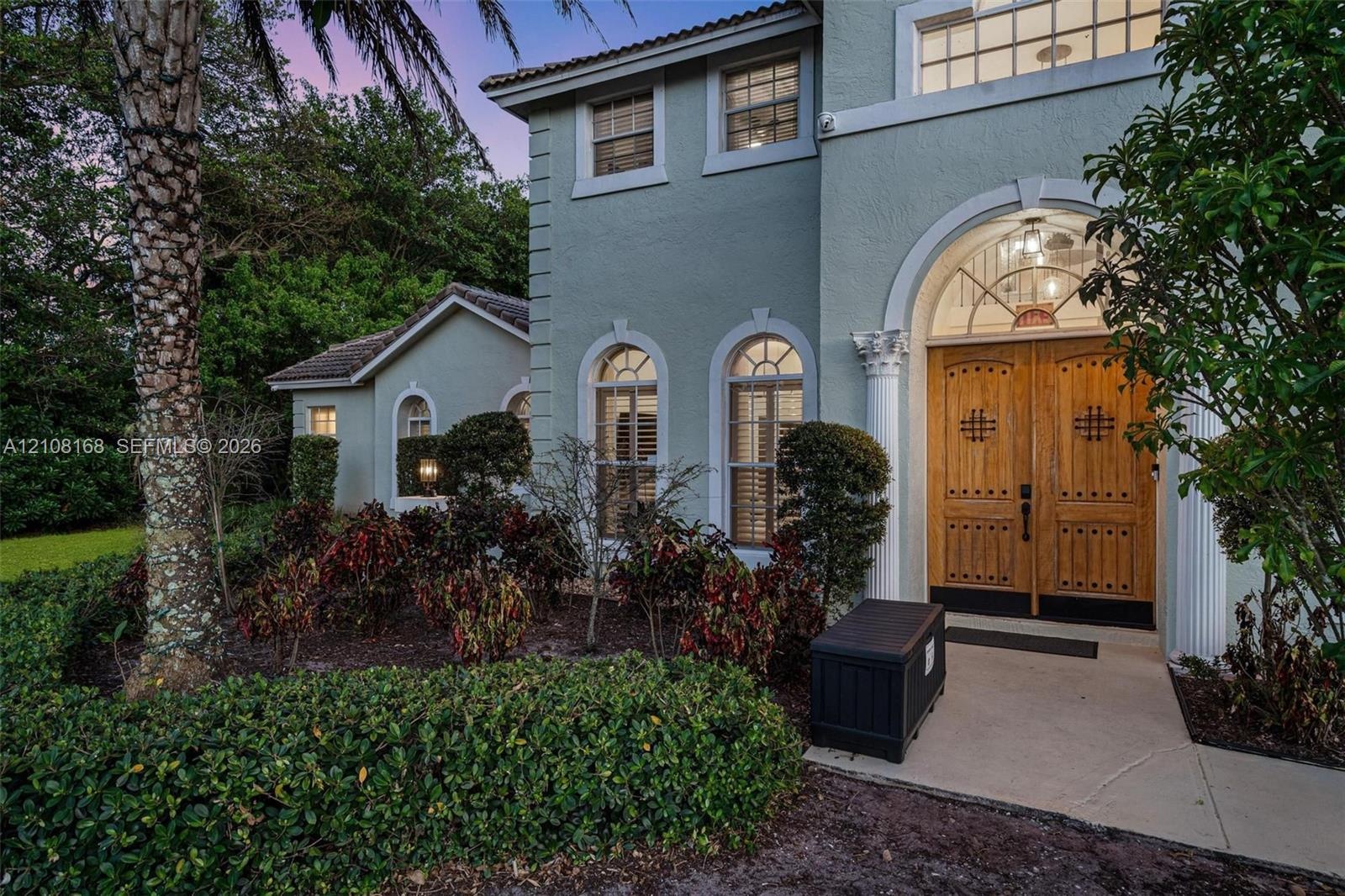 Stucco exterior featuring double arched wood front doors with decorative iron detailing, classical architectural columns, arched windows, and a paved 