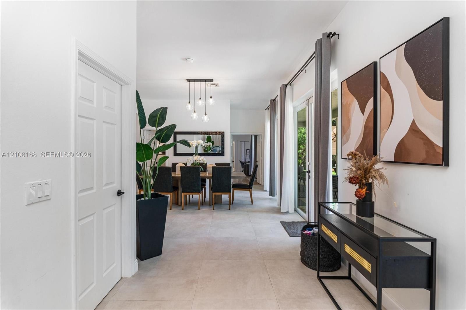 Large-format neutral floor tile, multi-light pendant chandelier, and sliding glass door with ceiling-mounted drapery hardware