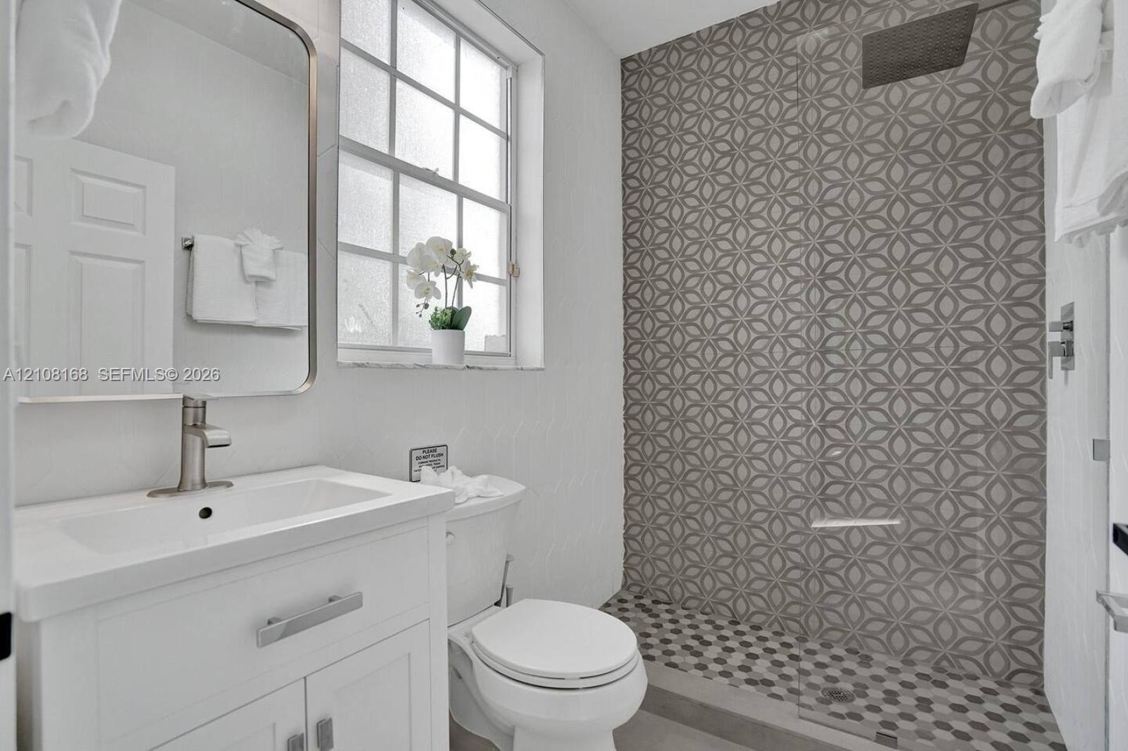 Bathroom featuring a white vanity cabinet with a rectangular basin, patterned geometric tilework in the walk-in shower, recessed ceiling-mounted showe