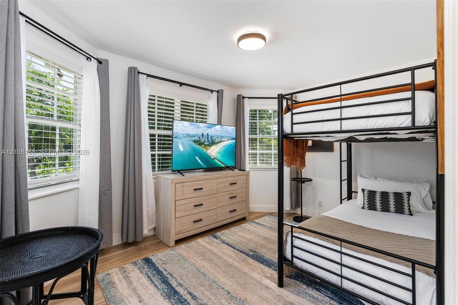 Bedroom featuring wood-finish flooring, three windows with plantation shutters, and a modern ceiling-mounted light fixture