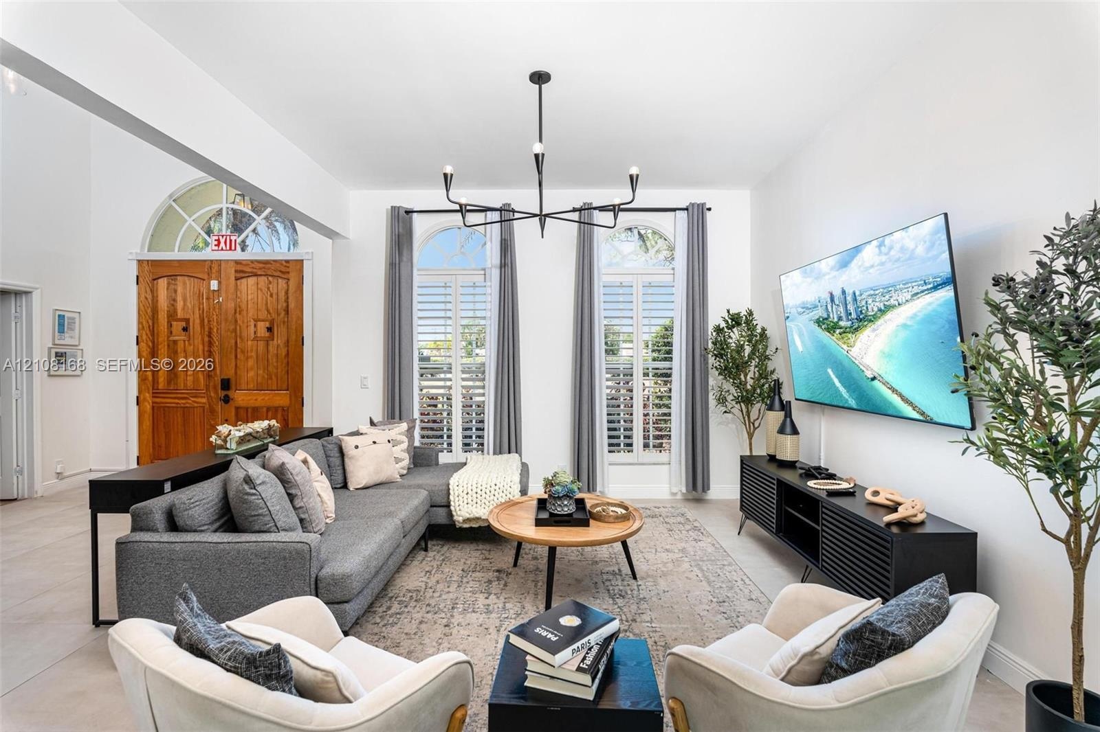 Living area featuring high ceilings, arched windows with plantation shutters, a multi-arm chandelier, and double wood entry doors with an arched trans