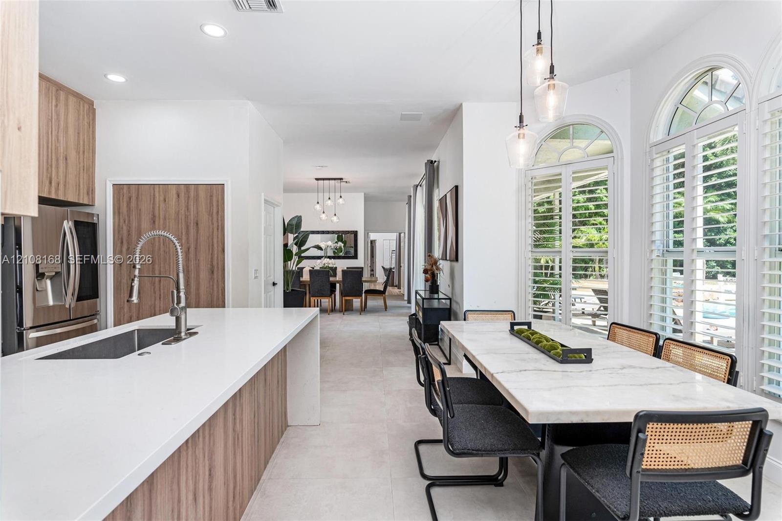 Kitchen featuring a large quartz-topped center island with integrated sink, wood-finish cabinetry, recessed lighting, and expansive arched windows wit