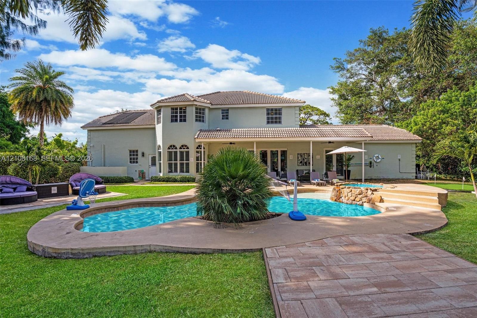 Backyard featuring a free-form swimming pool with a central island planter, raised stone-finished spa, expansive concrete pool decking, and a covered 