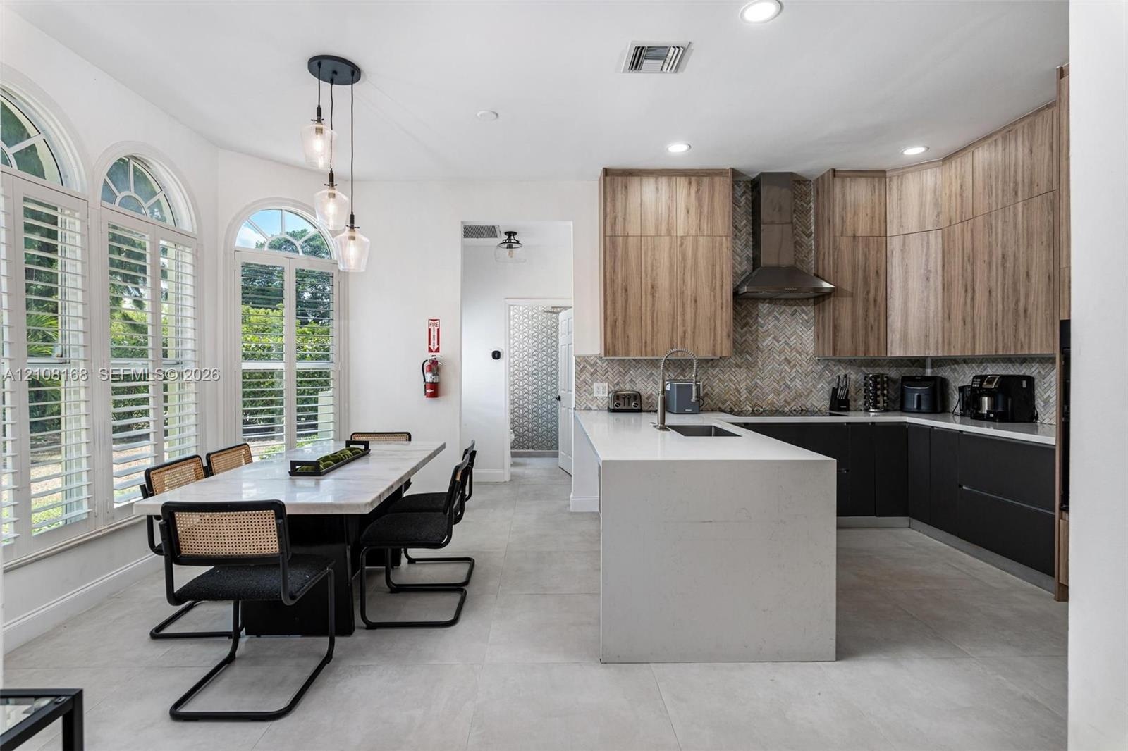 Kitchen featuring two-tone flat-panel cabinetry, a waterfall-edge center island, stainless steel range hood, herringbone tile backsplash, and arched w