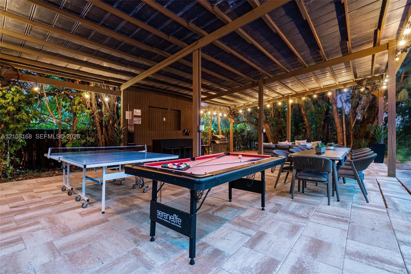 Covered outdoor patio featuring paver flooring, structural wood-beam framing, and integrated string lighting