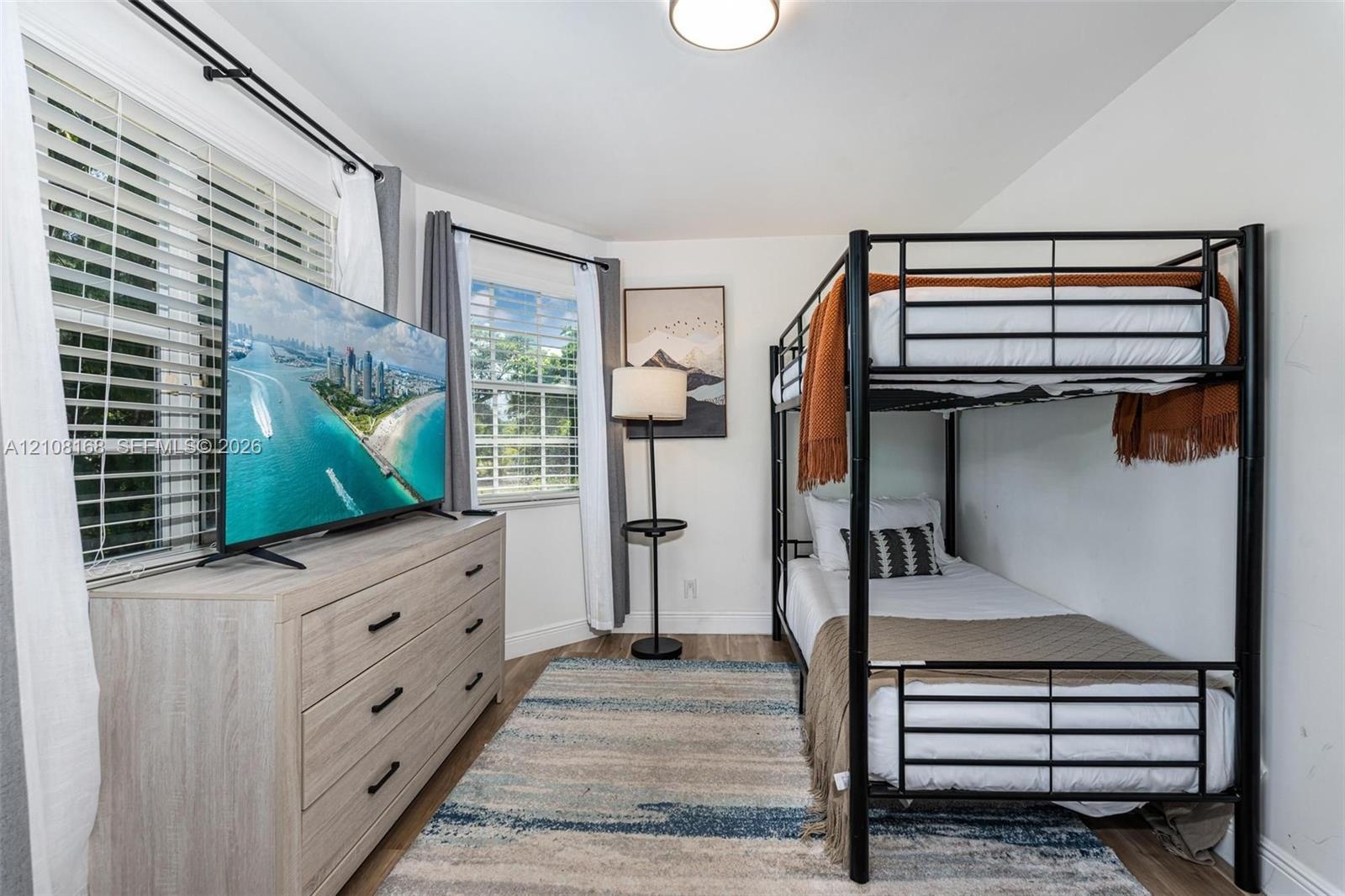 Room featuring wood-finish flooring, multiple windows with horizontal blinds, and a flush-mount overhead light fixture