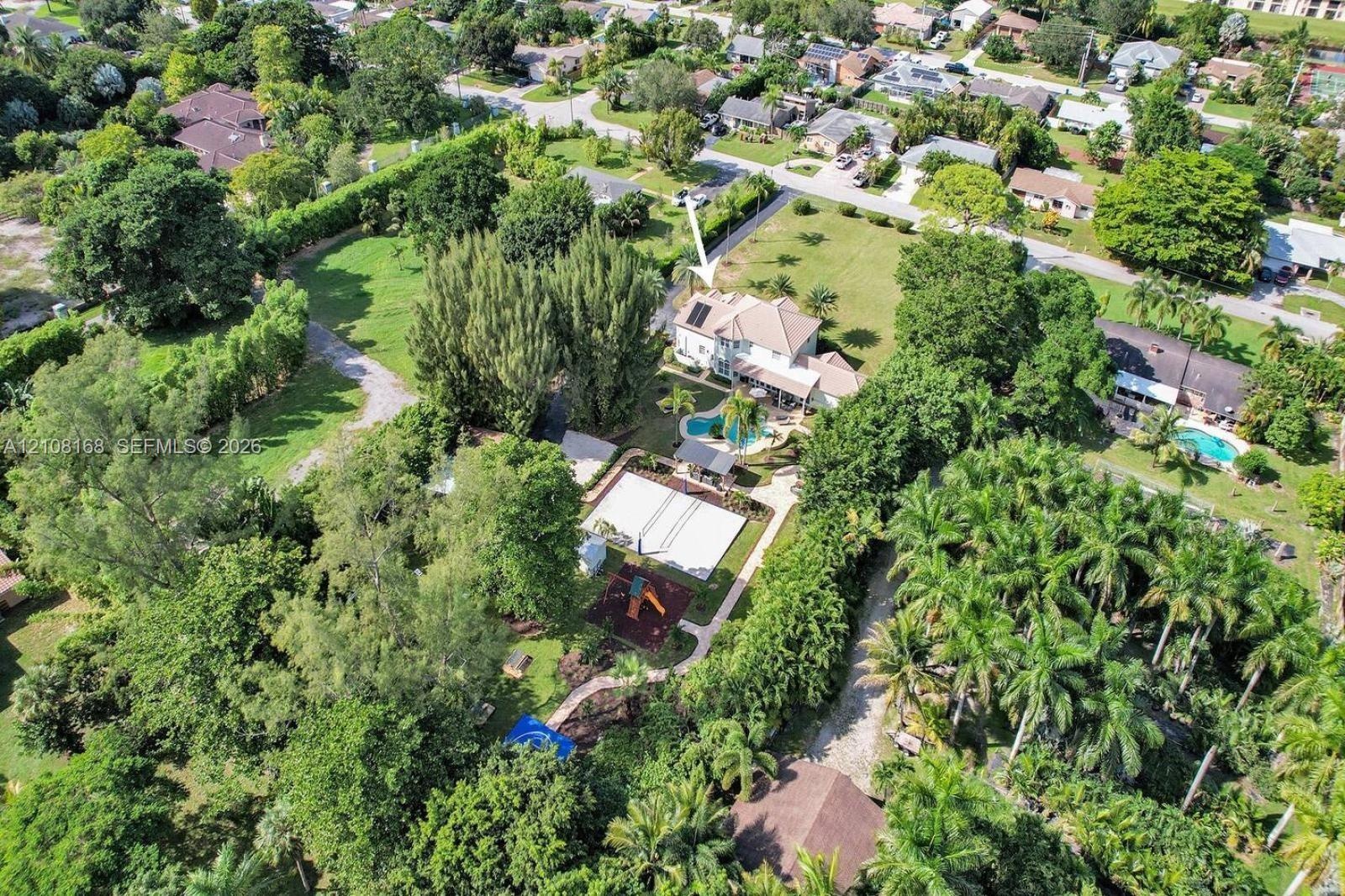 Aerial perspective of a multi-story residence featuring an in-ground swimming pool, a hardscaped sport court, extensive mature landscaping, and solar 