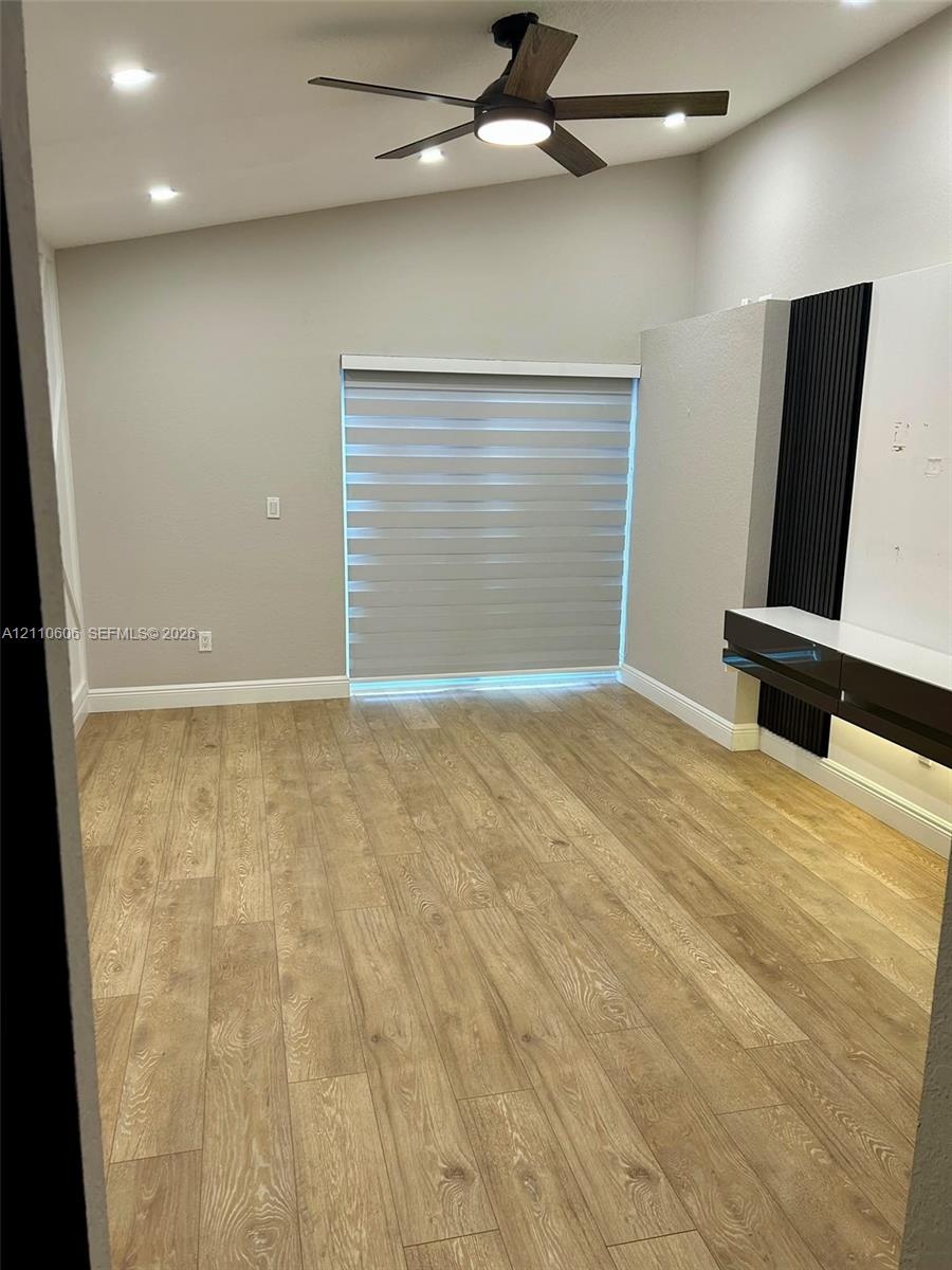 Wood-finish flooring, vaulted ceilings, recessed lighting, ceiling fan with integrated lighting, and a built-in media console featuring vertical accen
