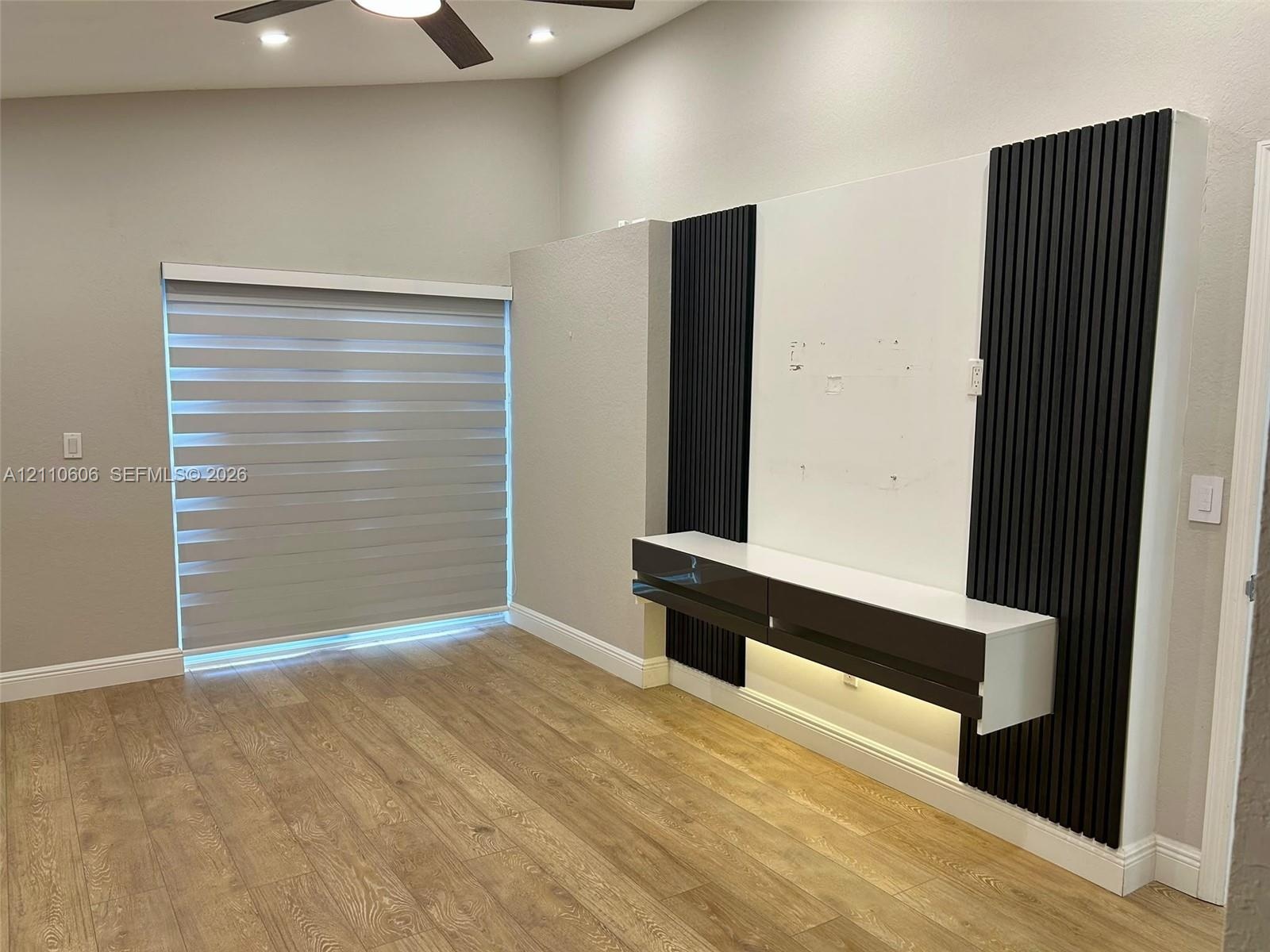 Vaulted ceiling featuring a ceiling fan, wood-finish flooring, and a custom built-in media console with black vertical accent paneling and integrated 