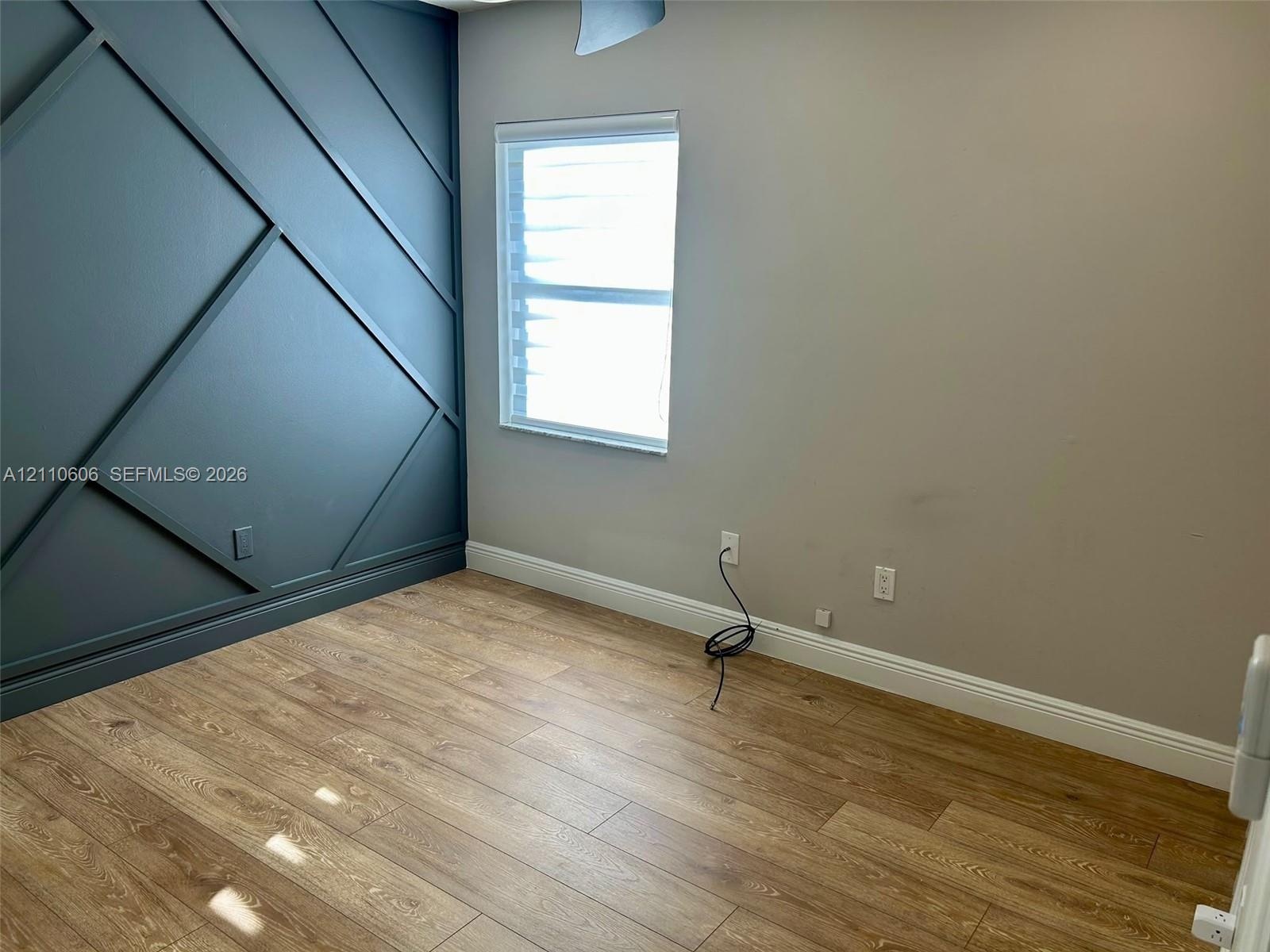 Room featuring an accent wall with geometric millwork, wood-finish flooring, and a window with horizontal blinds