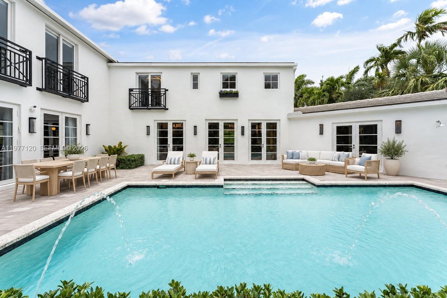 Stucco exterior featuring multiple sets of French doors, a stone-paved patio, an in-ground swimming pool with water features, and iron-railed balconie