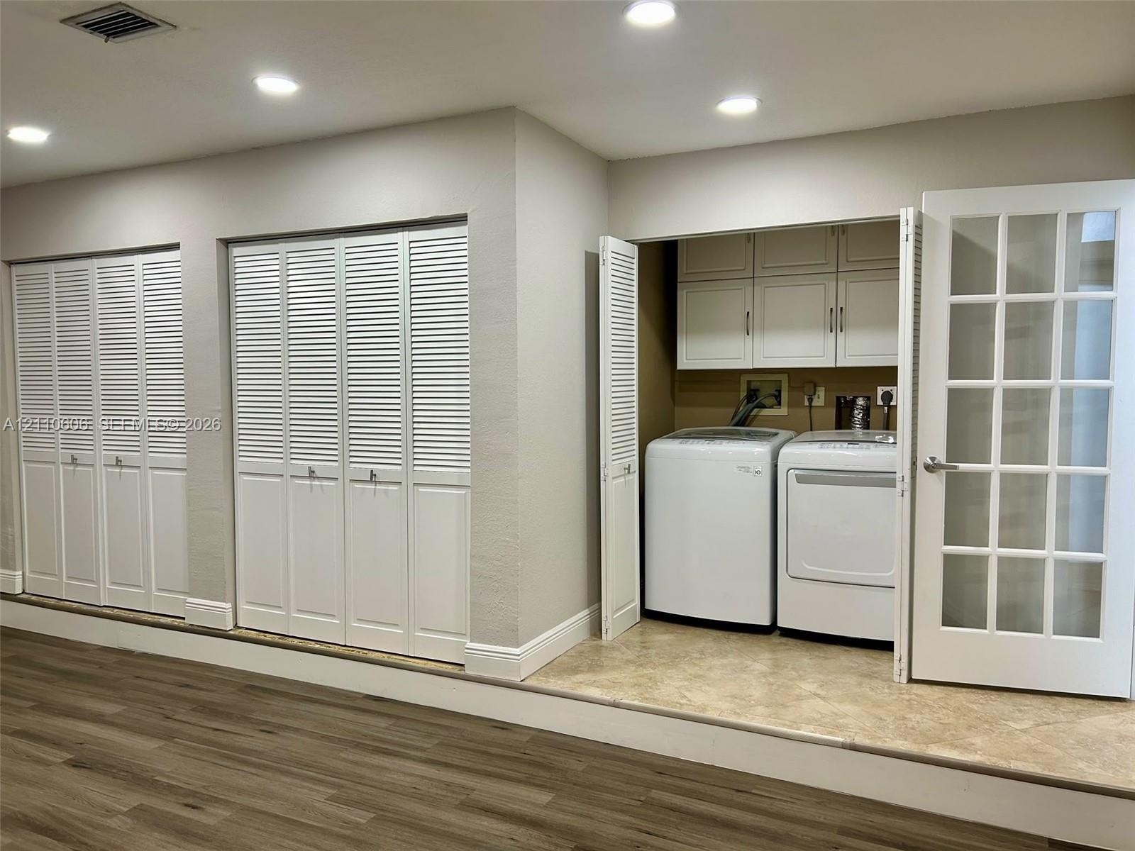 Laundry area featuring built-in cabinetry, recessed lighting, and louvered closet doors, set on a raised tile platform with wood-finish flooring in th