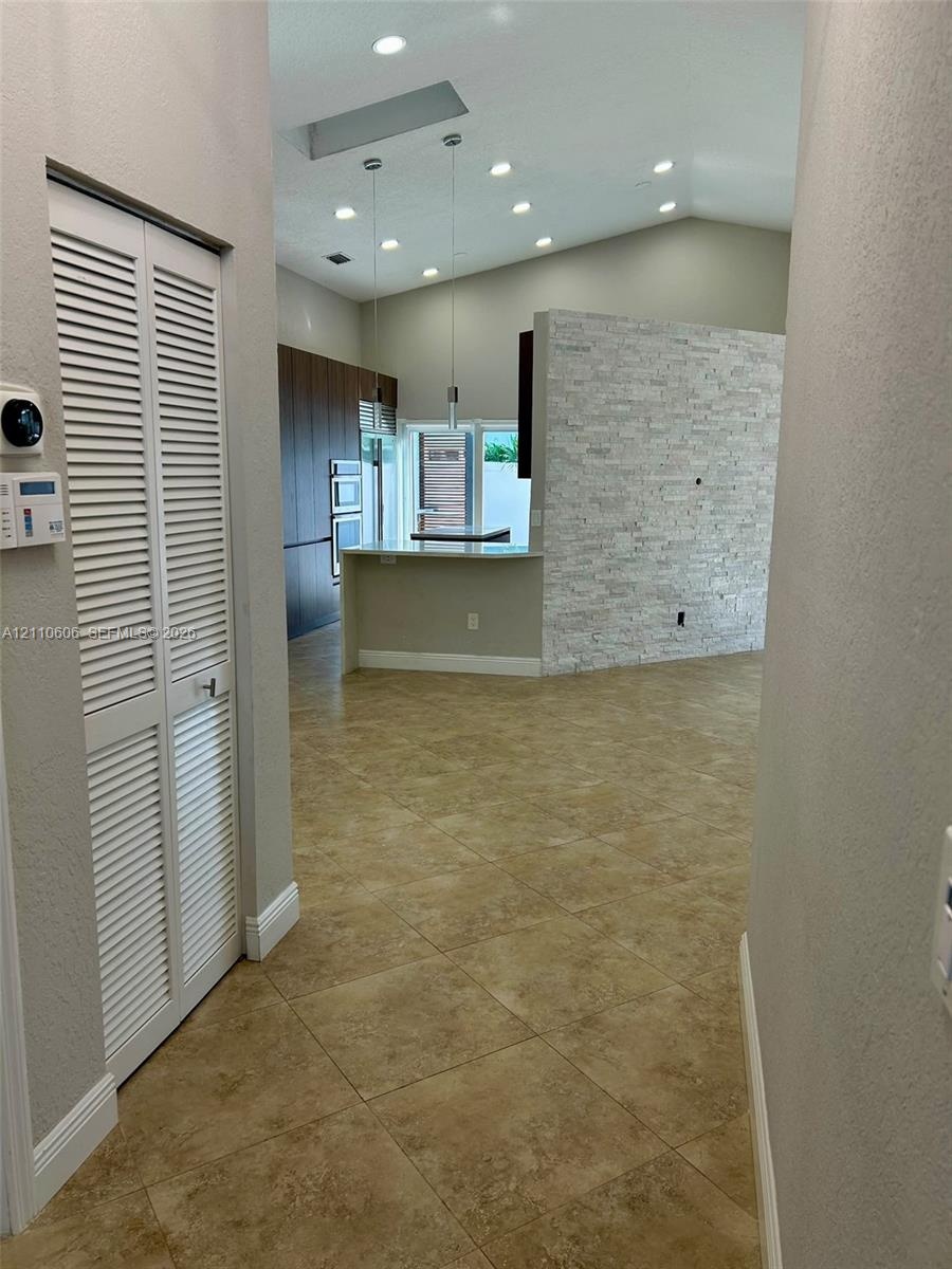 Open-concept space featuring vaulted ceilings, recessed lighting, a stone-veneer accent wall, tile flooring, and built-in cabinetry
