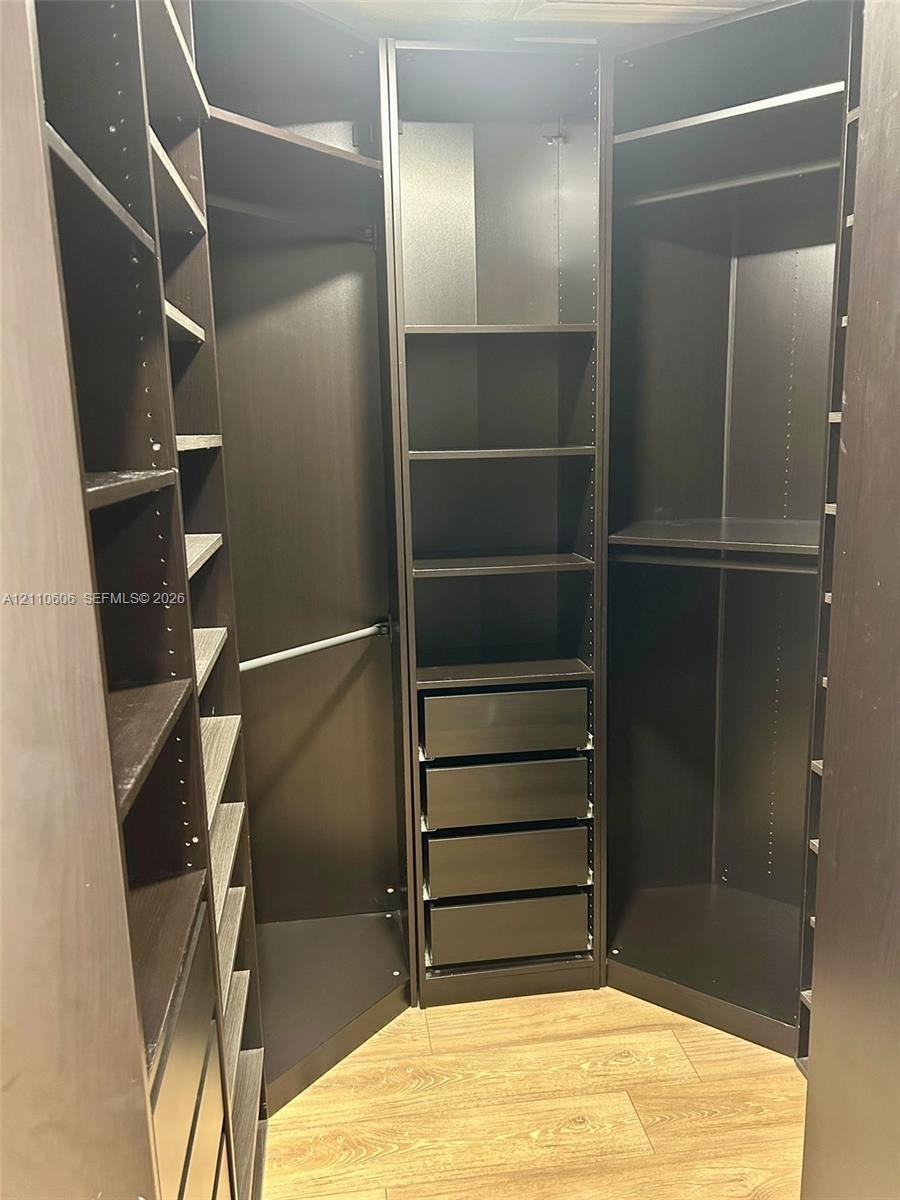 Custom walk-in closet featuring floor-to-ceiling dark cabinetry, adjustable shelving, integrated drawer stack, metal garment rods, and wood-finish flo
