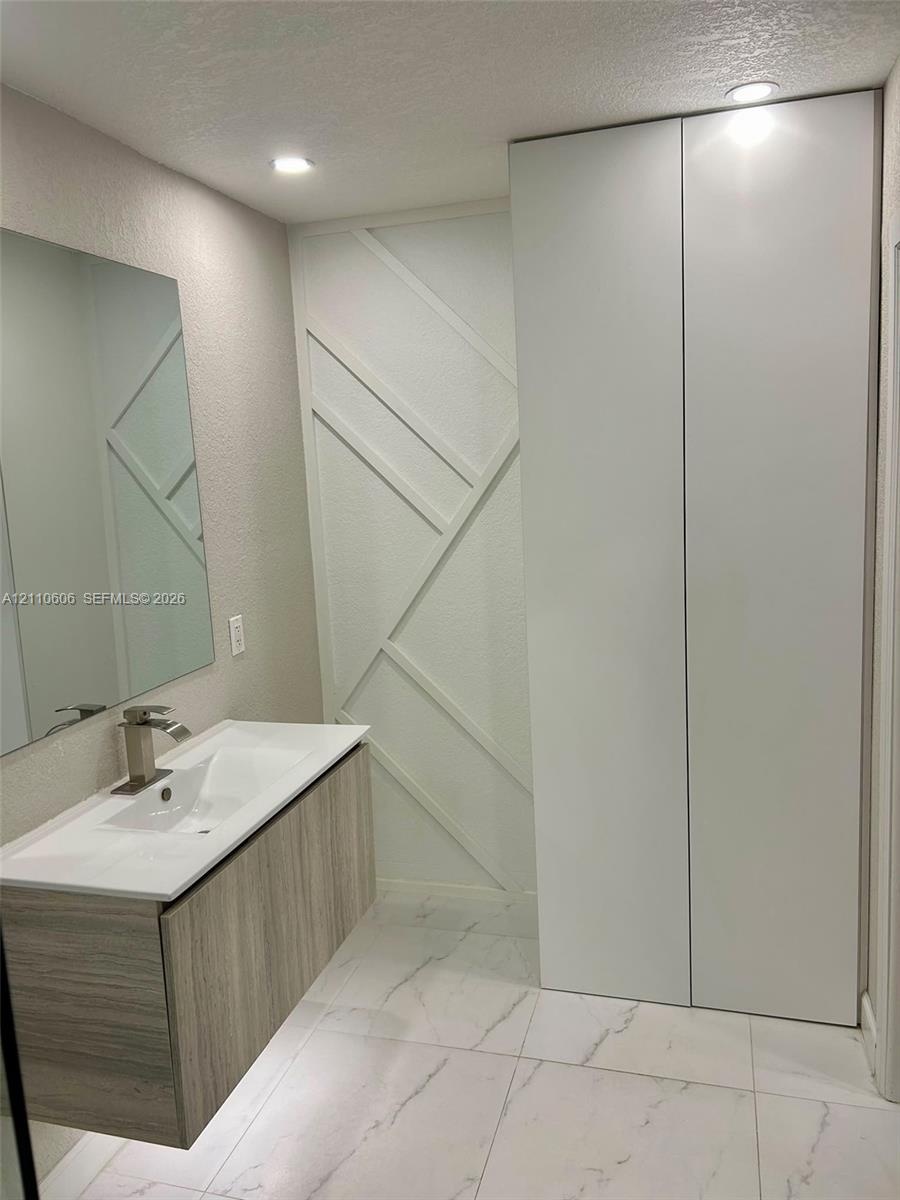 Floating vanity with wood-finish cabinetry, white countertop, integrated sink, and matte metallic faucet, complemented by full-height floor-to-ceiling