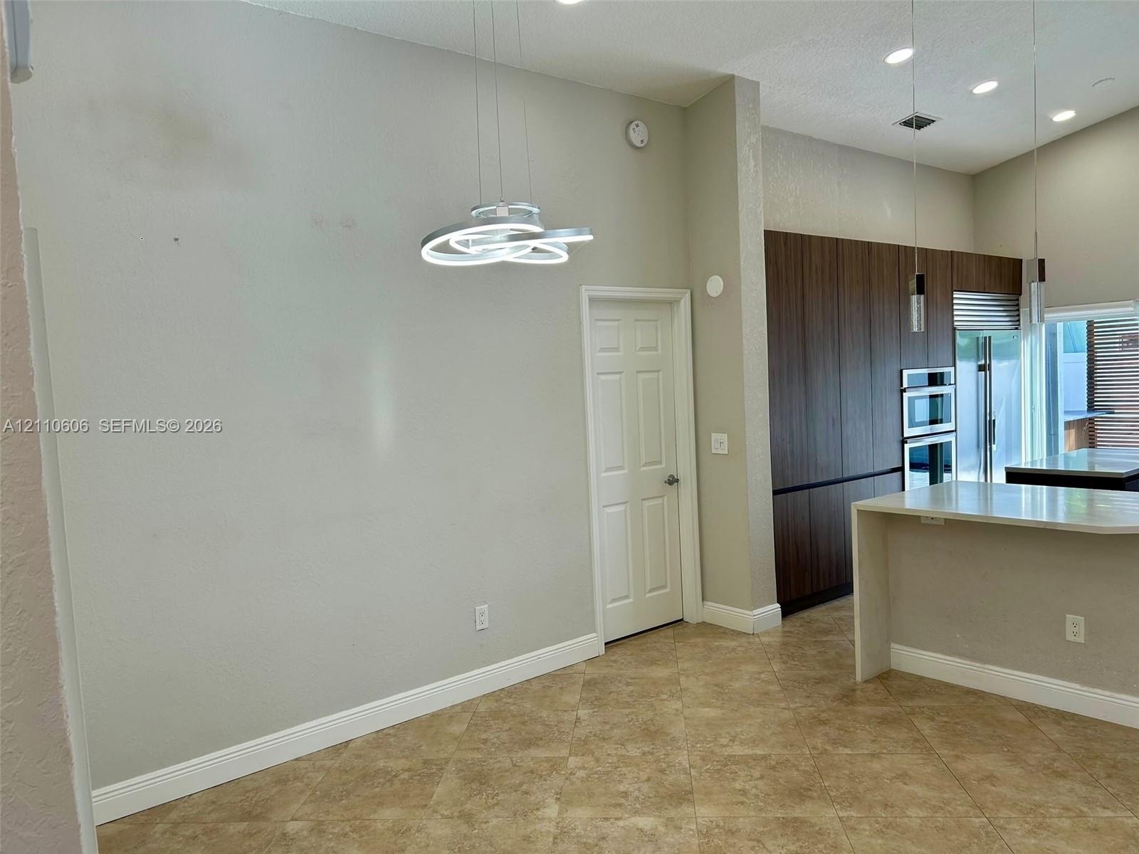 Vaulted ceilings featuring modern sculptural pendant lighting, stone-finish tile flooring, floor-to-ceiling wood-finish cabinetry, and recessed lighti