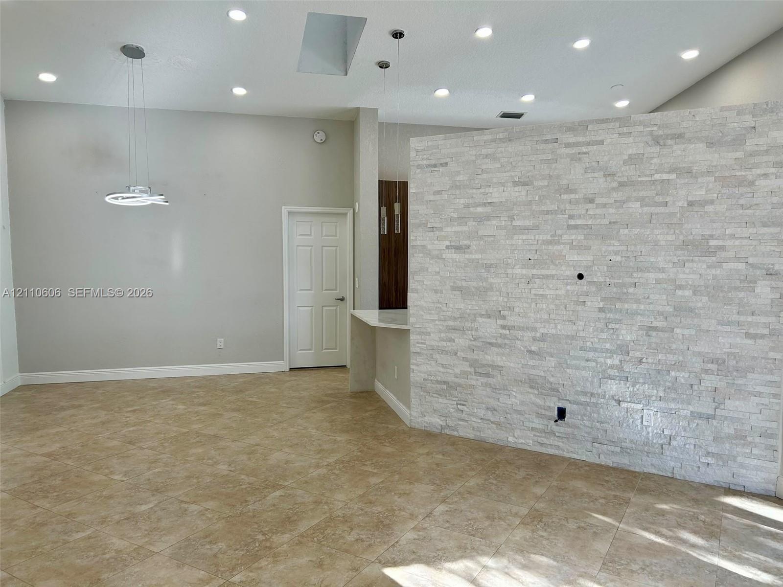 Stacked stone accent wall, recessed lighting, polished tile flooring, skylight, and modern pendant lighting