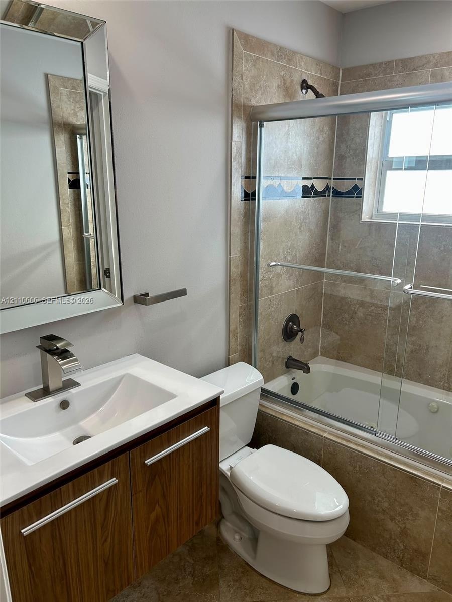 Bathroom featuring a wood-finish vanity with a rectangular sink, beveled-edge wall mirror, and a tiled shower-tub combination with a sliding glass doo