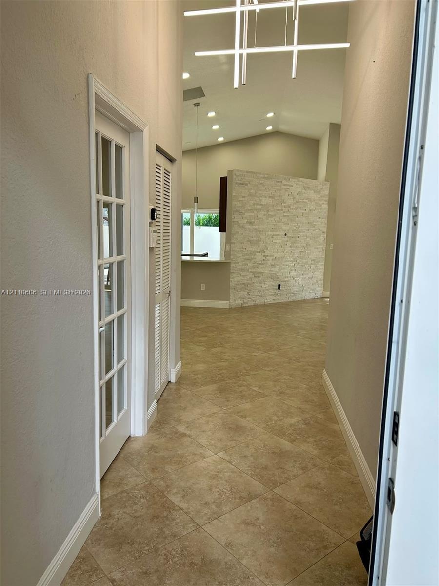 Entryway featuring tile flooring, vaulted ceilings, a stacked stone accent wall, recessed lighting, and a linear modern chandelier